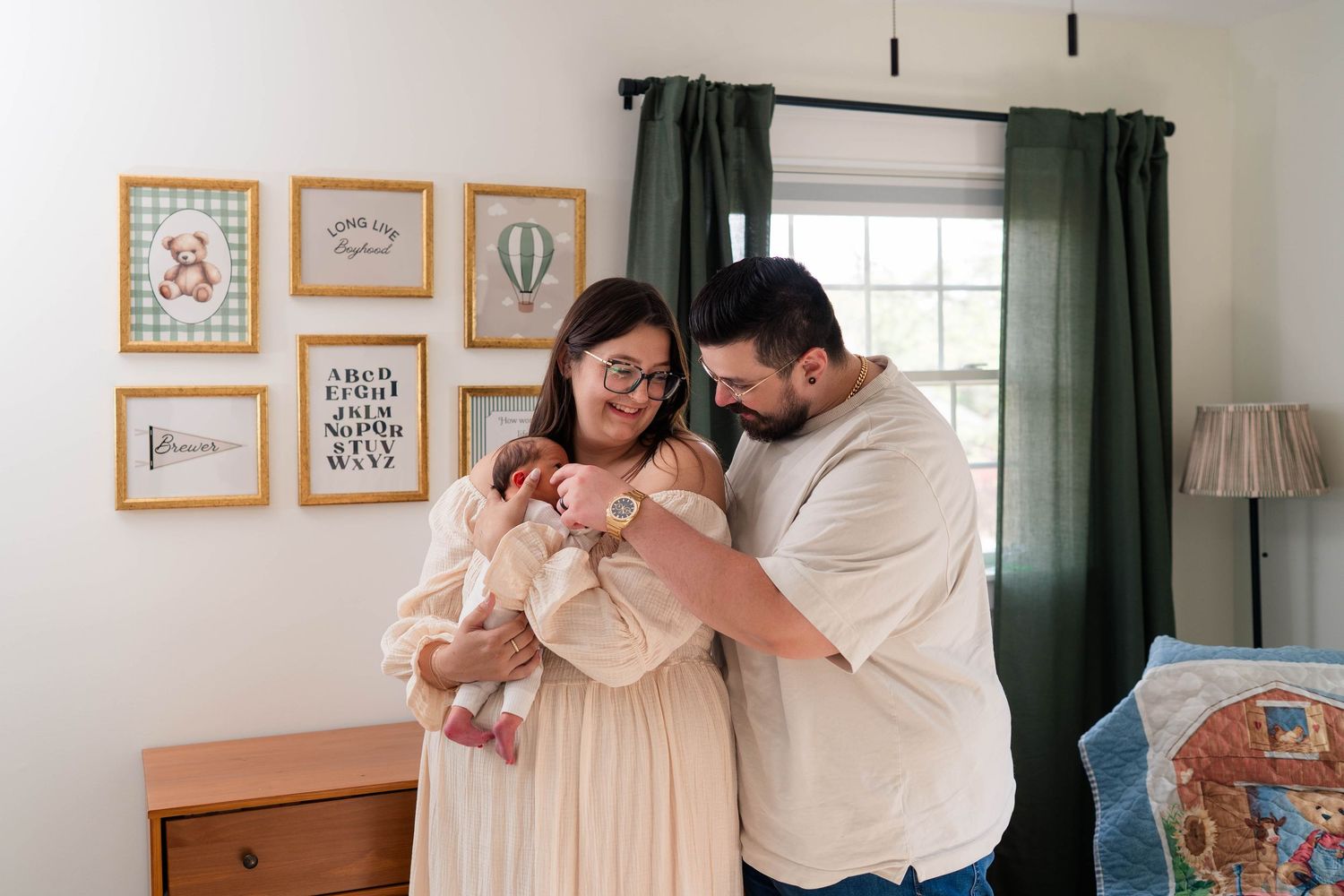 New parents stand together in decorated nursery lovingly gazing down at their newborn baby.