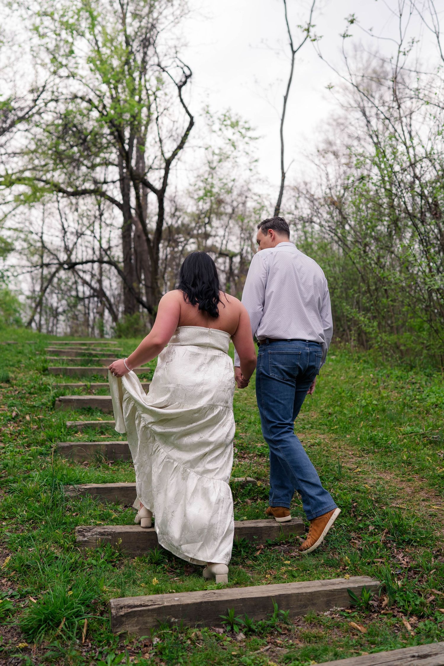 Couple holding hands walking up wooden steps through a green park landscape.