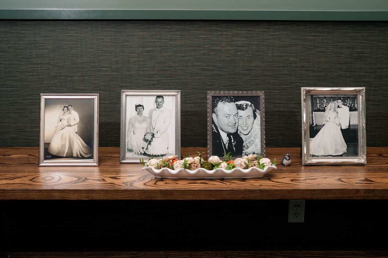 Four vintage black and white wedding photos displayed on wooden table with floral arrangement.