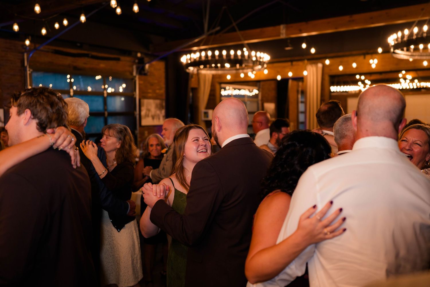 Guests dancing and celebrating together under string lights at a lively wedding reception.