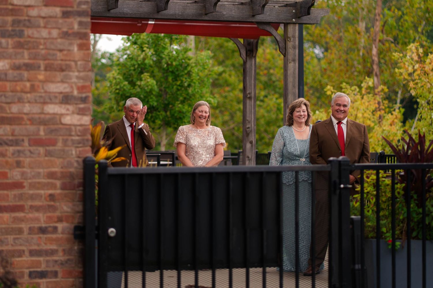 Four family members smiling on balcony at outdoor wedding venue surrounded by trees.