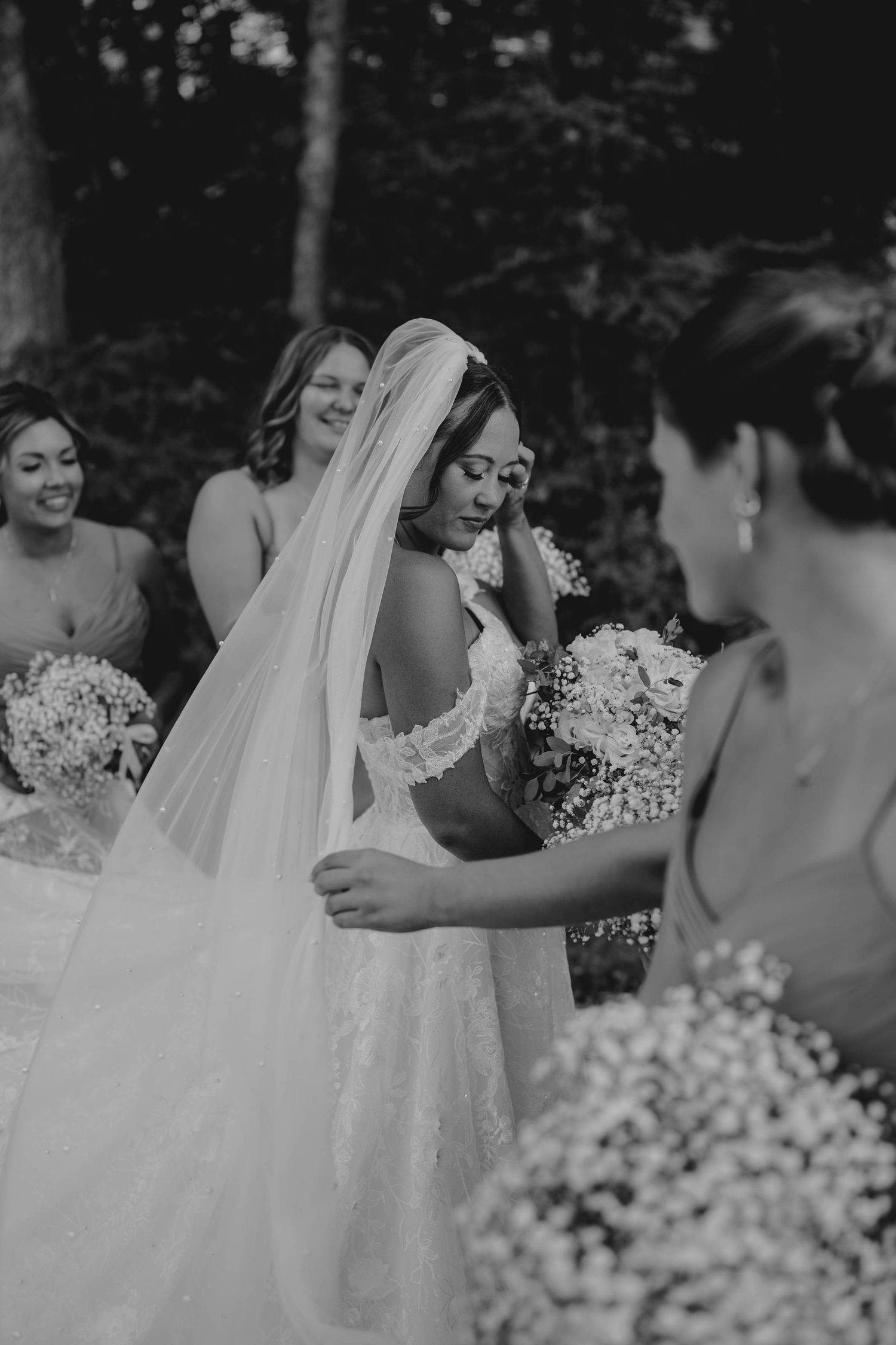 Black and white photo of emotional bride in lace gown and veil surrounded by bridesmaids holding bouquets.