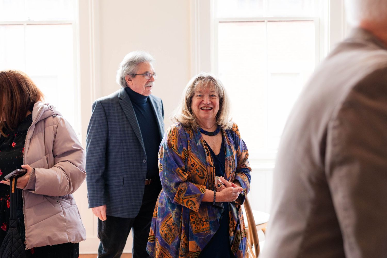 Two guests smile and laugh together at a formal indoor event, woman wearing colorful patterned shawl.