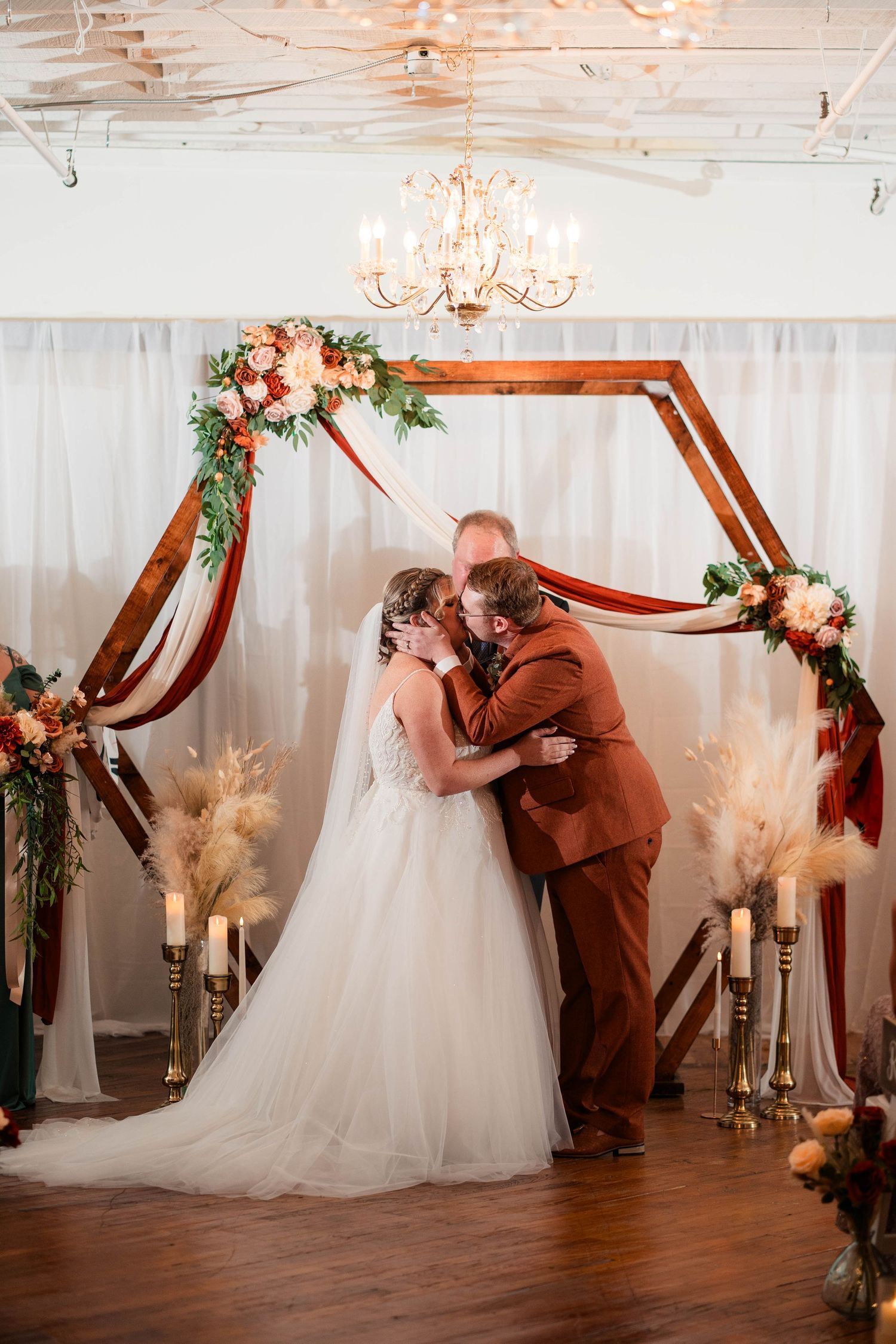 Bride and groom share first kiss under a hexagonal wooden arch with floral and pampas decor.