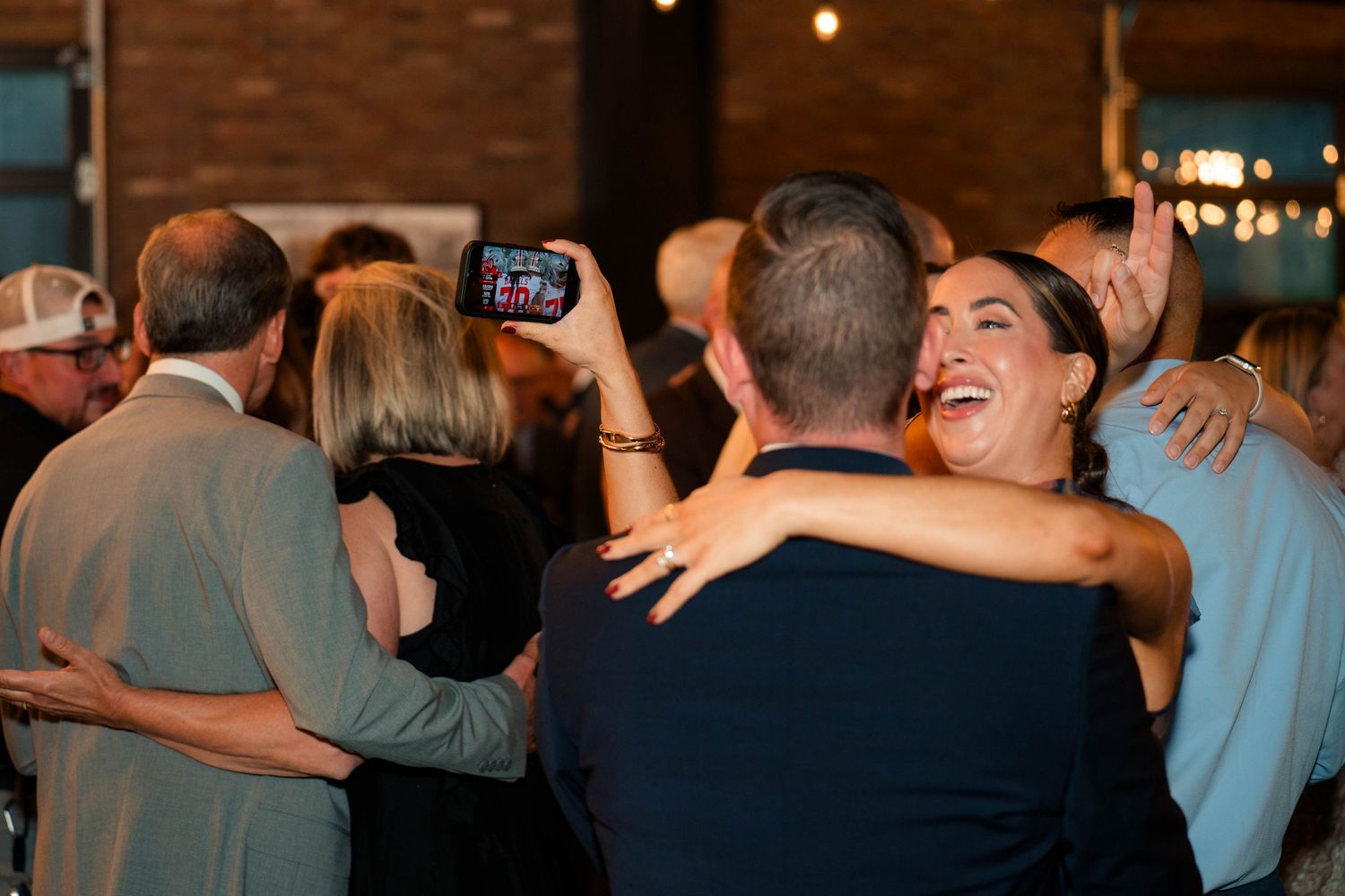 Guests laugh and embrace joyfully on the dance floor at a wedding reception.