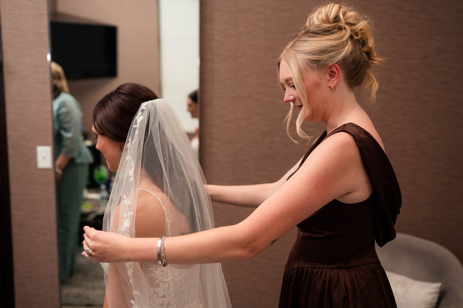 Blonde bridesmaid in black dress carefully arranging brides veil before wedding ceremony.