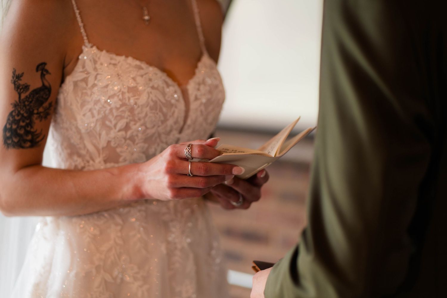 Bride with tattoos reading vows while holding grooms hands during intimate wedding ceremony.