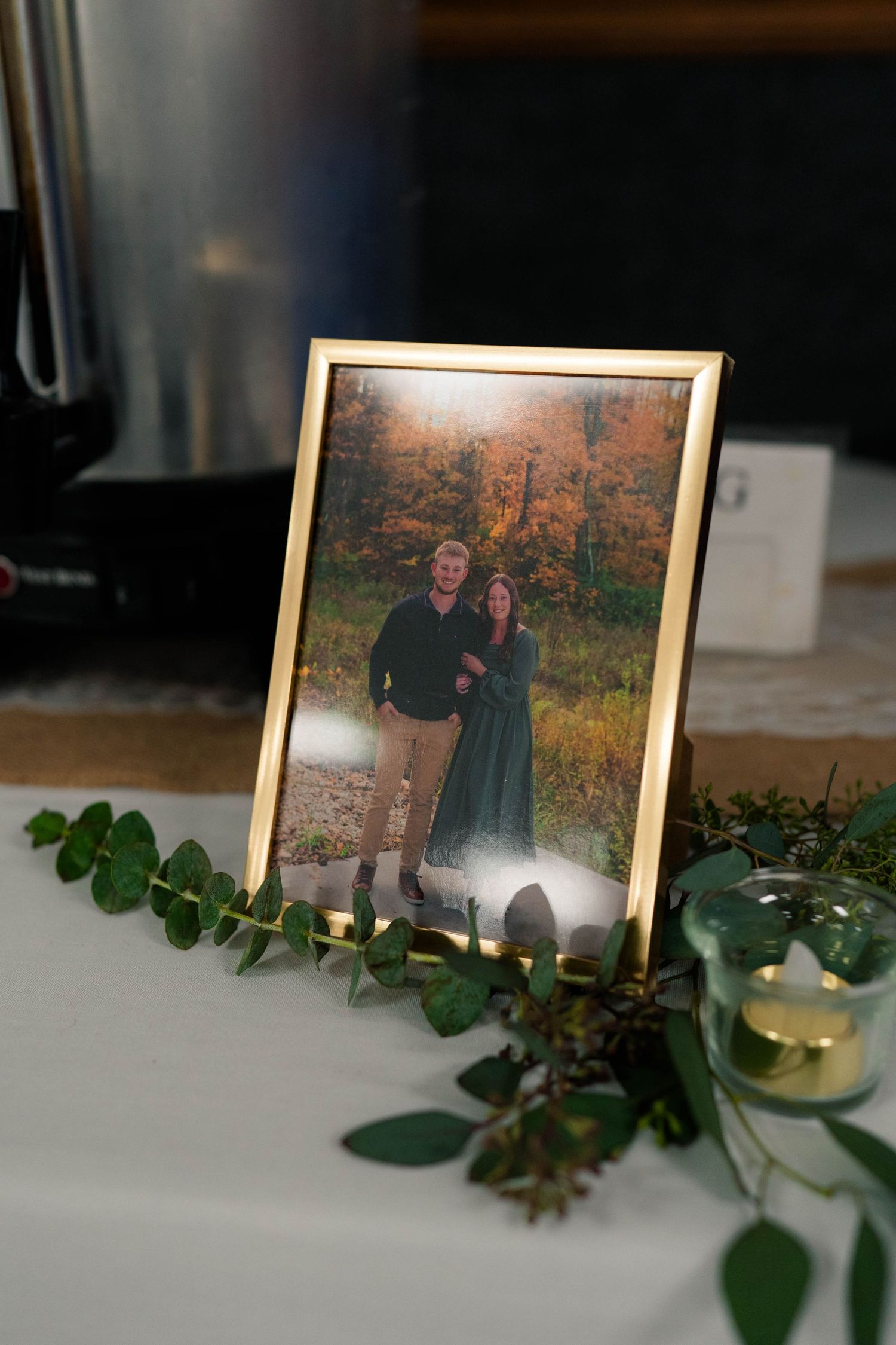 Gold framed engagement photo of couple in autumn setting on decorated table.