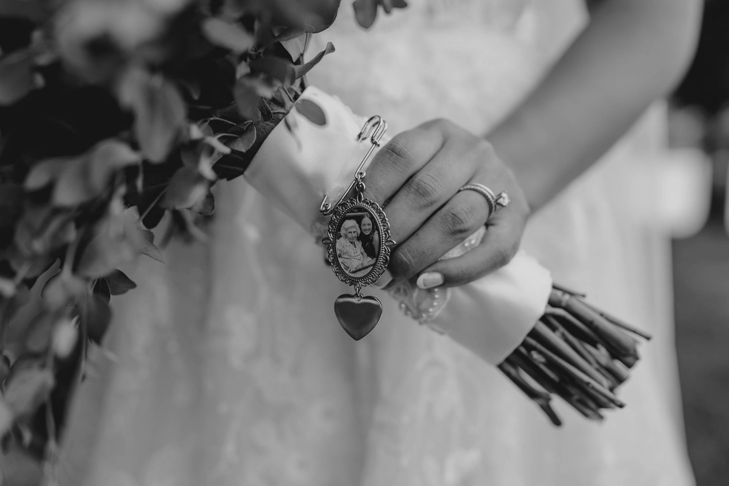 Black and white close-up of bride holding bouquet with a heart locket charm bracelet on her wrist.