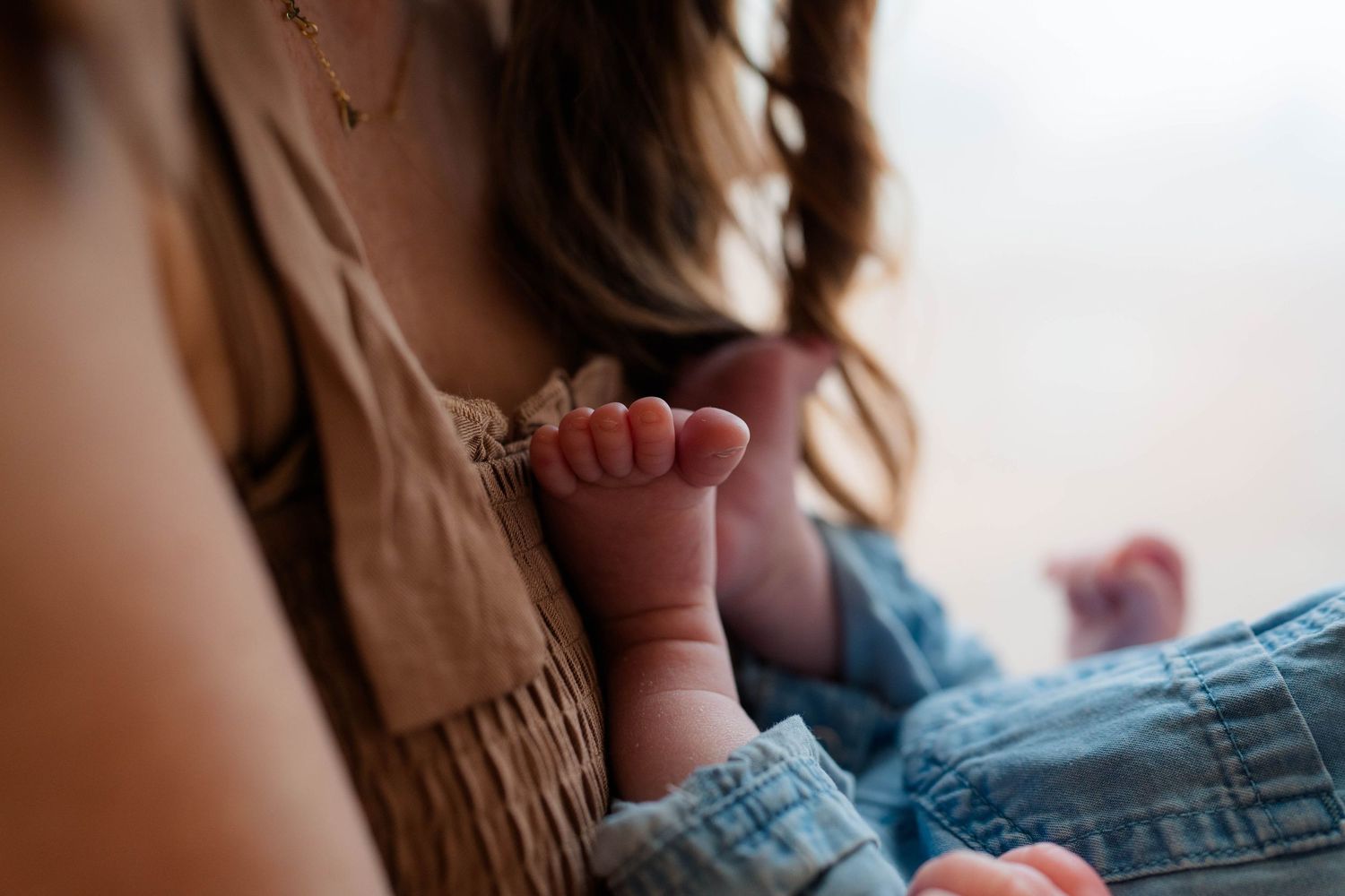 Mother holding her newborn baby's tiny feet while wearing a fringed boho top and jeans.