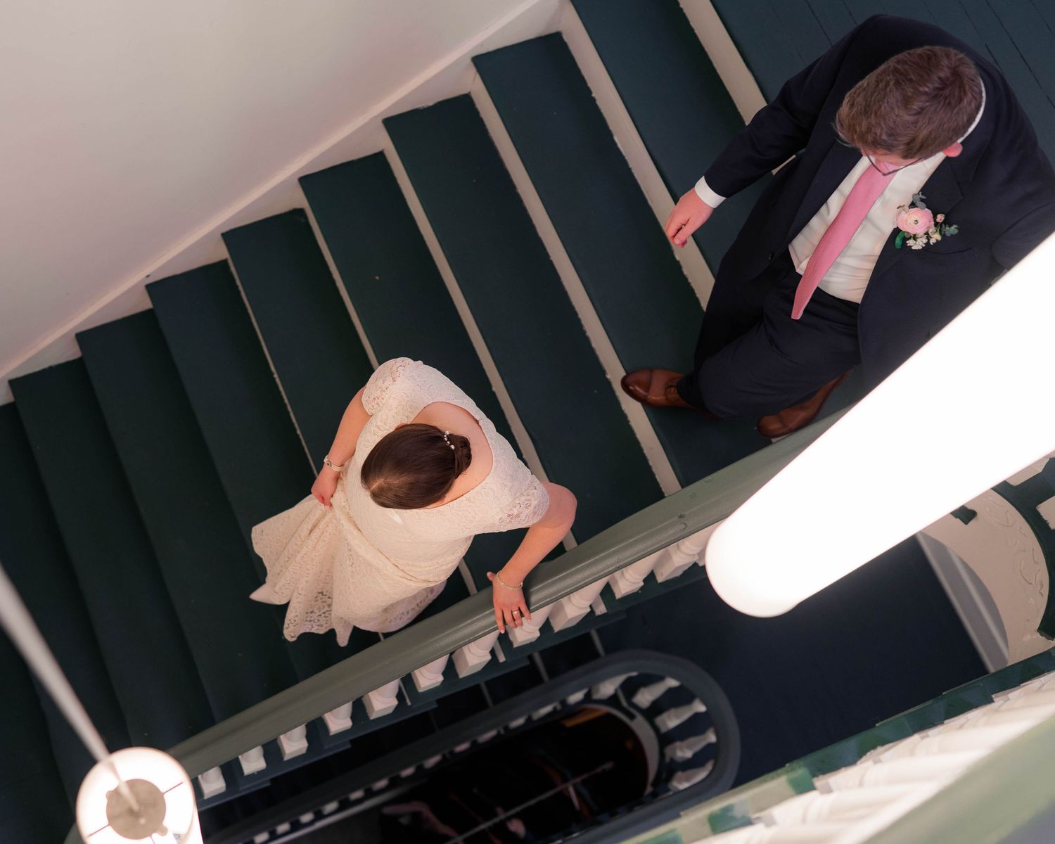 Aerial view of bride and groom descending elegant dark green staircase at wedding venue.
