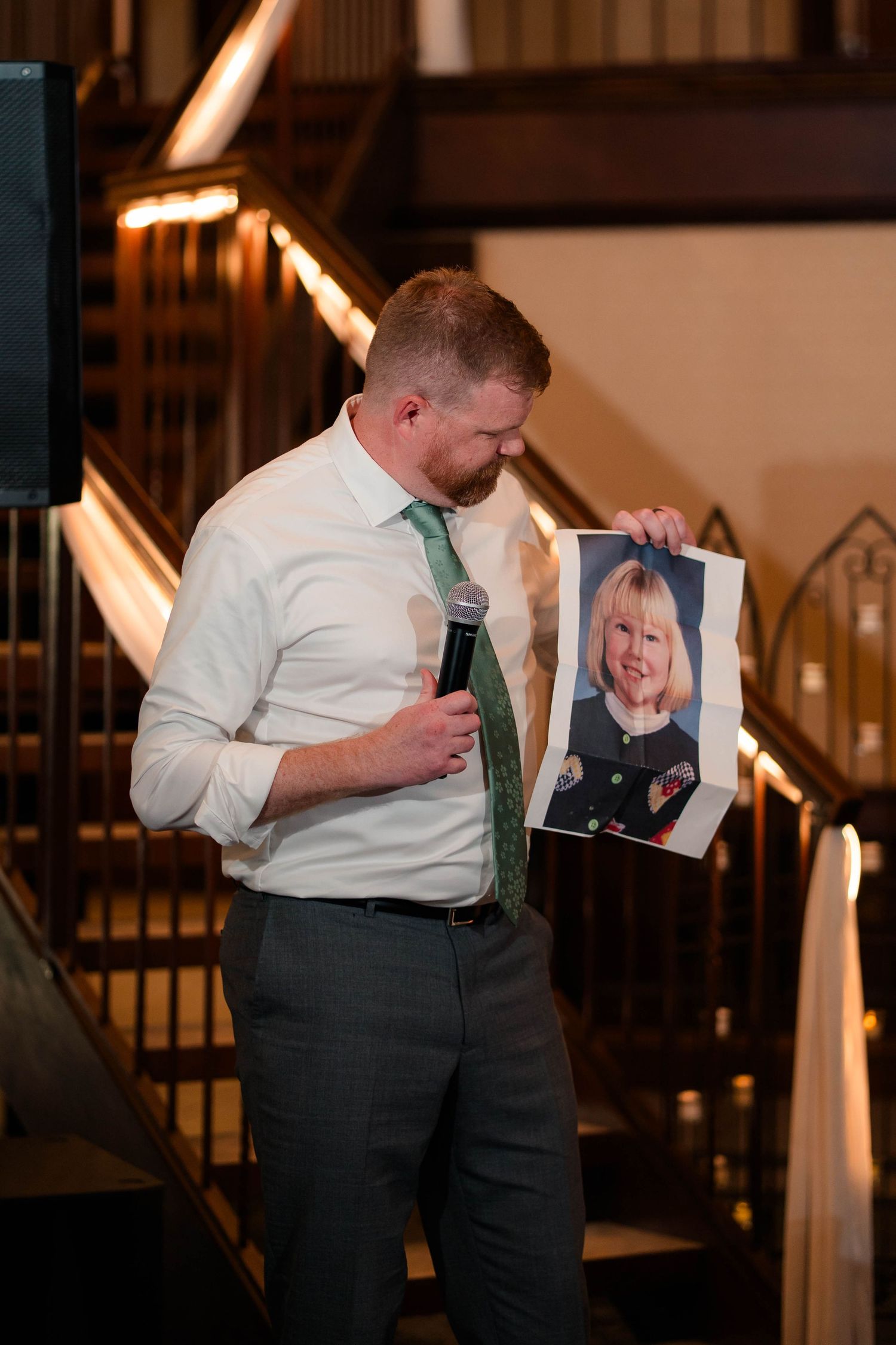 Best man holds childhood photo while giving speech at wedding reception.
