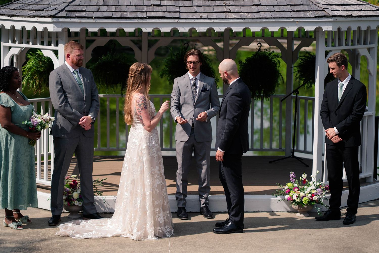 Bride and groom exchange vows at an outdoor gazebo wedding ceremony with attendants.