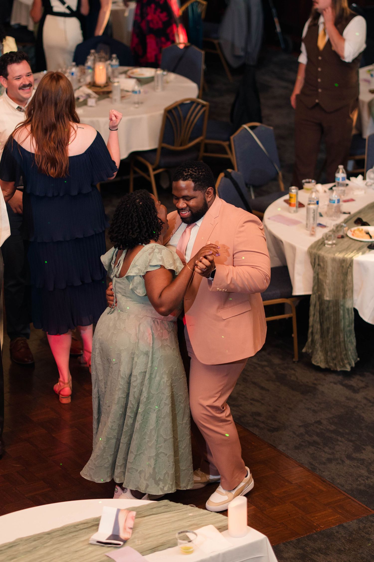Couple in pink suit and green dress share a joyful dance at a wedding reception.