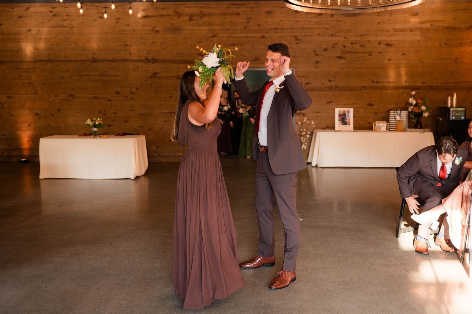 Bridesmaid in mauve dress dancing with groomsman on wooden dance floor at wedding reception.