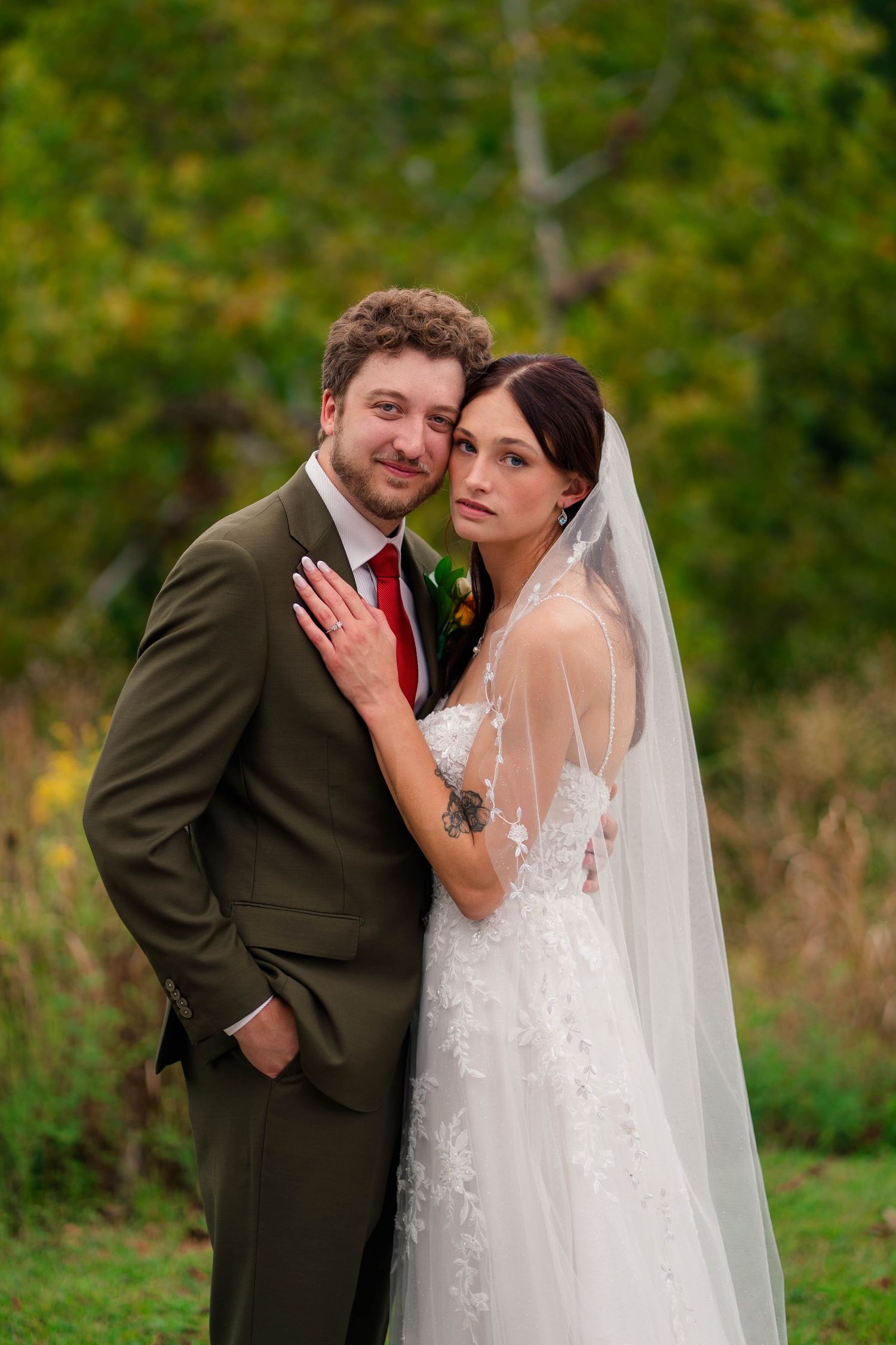 Bride and groom embrace outdoors in autumn setting, bride wearing lace gown and veil.