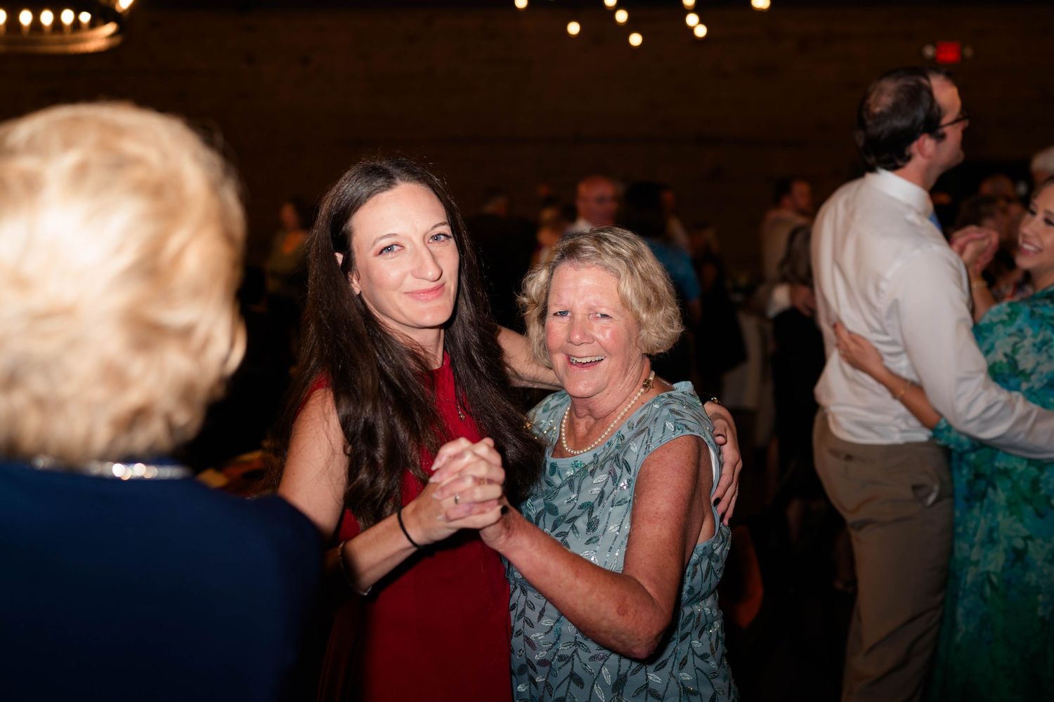 Two women smile and dance together joyfully at lively wedding reception celebration.