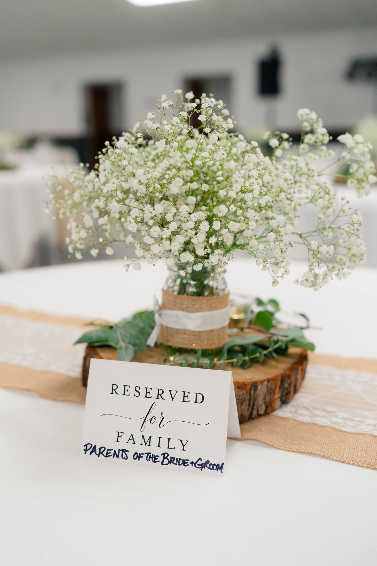 Rustic wedding centerpiece with baby's breath in burlap vase on wood slice with reserved family sign.