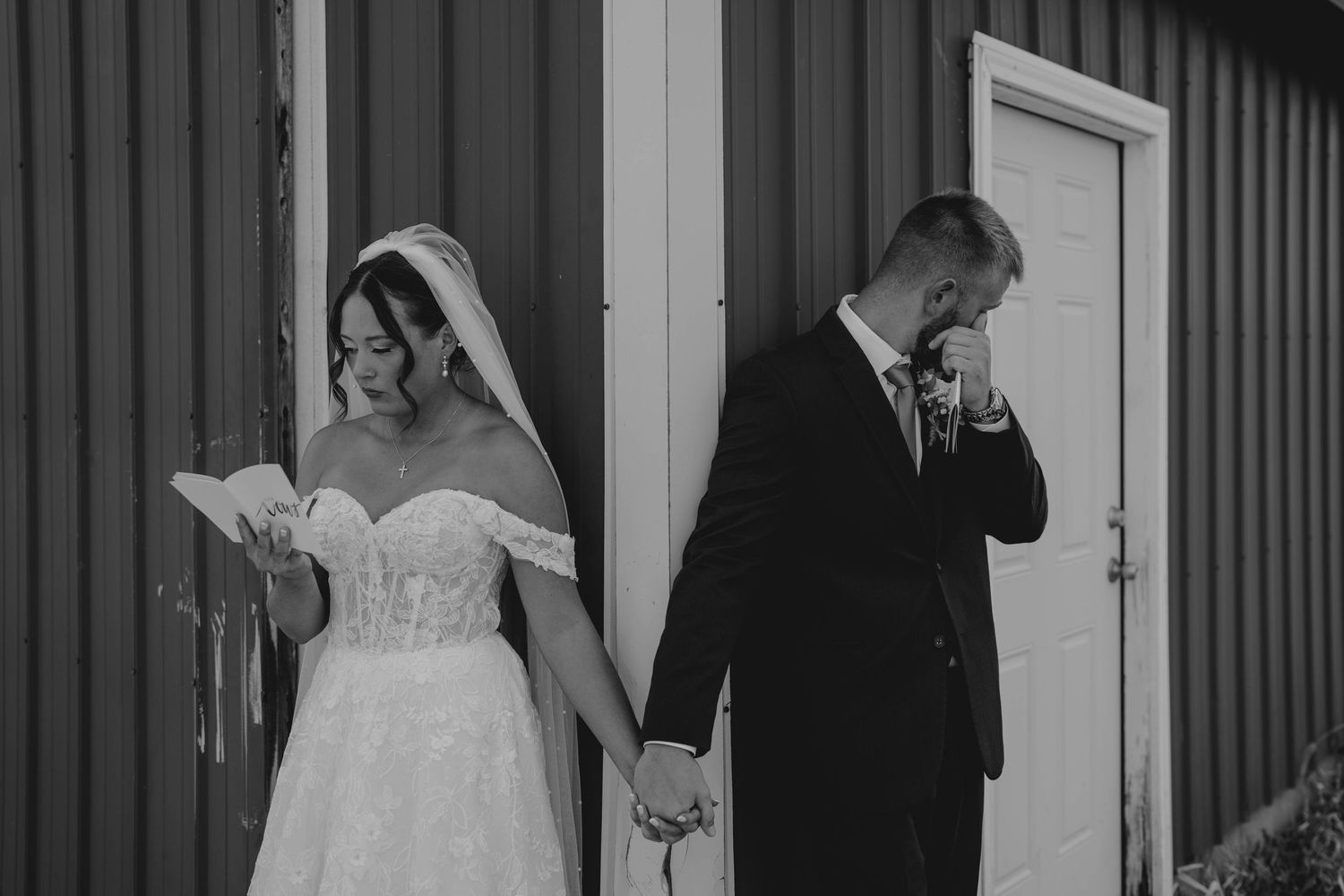 Emotional black and white photo of bride and groom reading vows during first look at red barn.