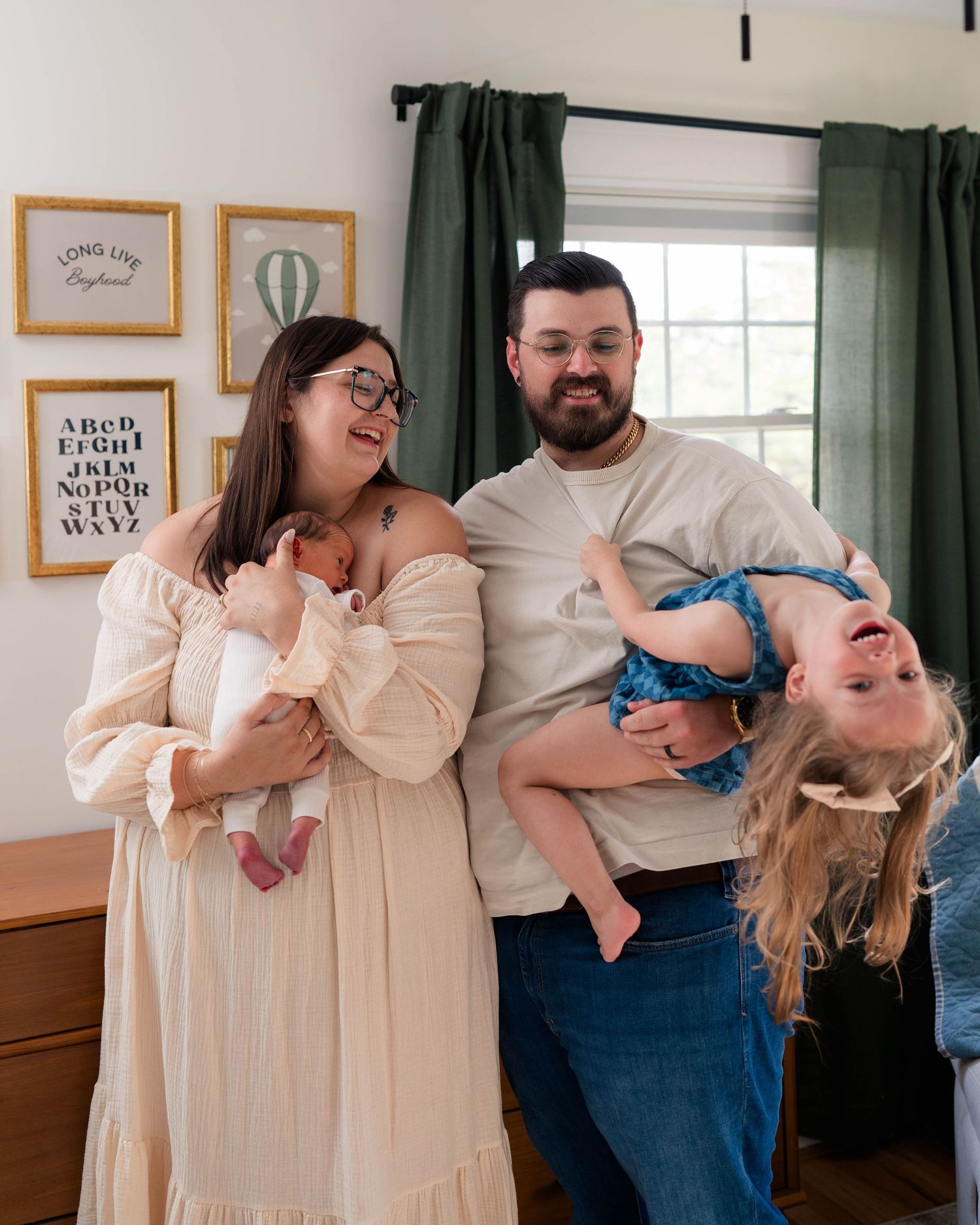 Joyful family portrait with parents holding newborn and playfully flipping toddler upside down.