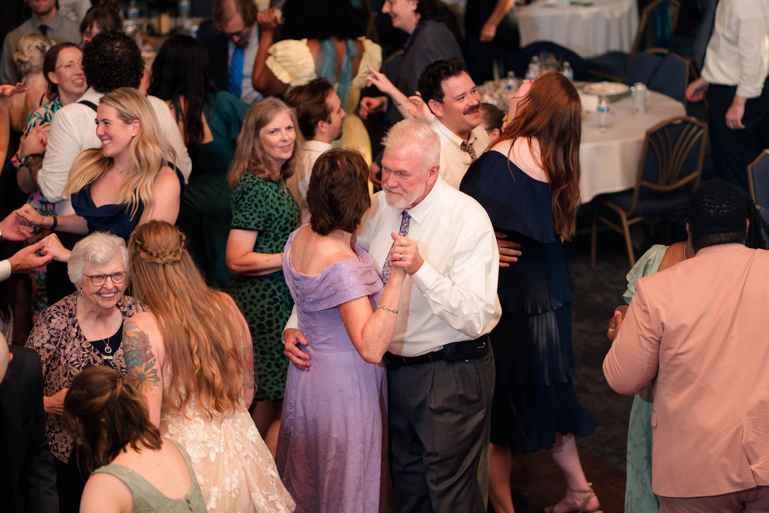 Wedding guests enjoy open dance floor celebration in elegant reception venue with warm lighting.