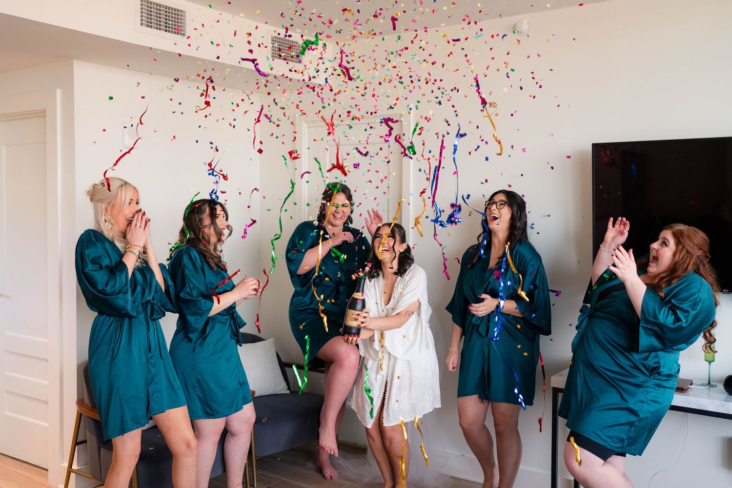 Bridesmaids in teal robes celebrate with confetti and champagne during bridal party getting ready.