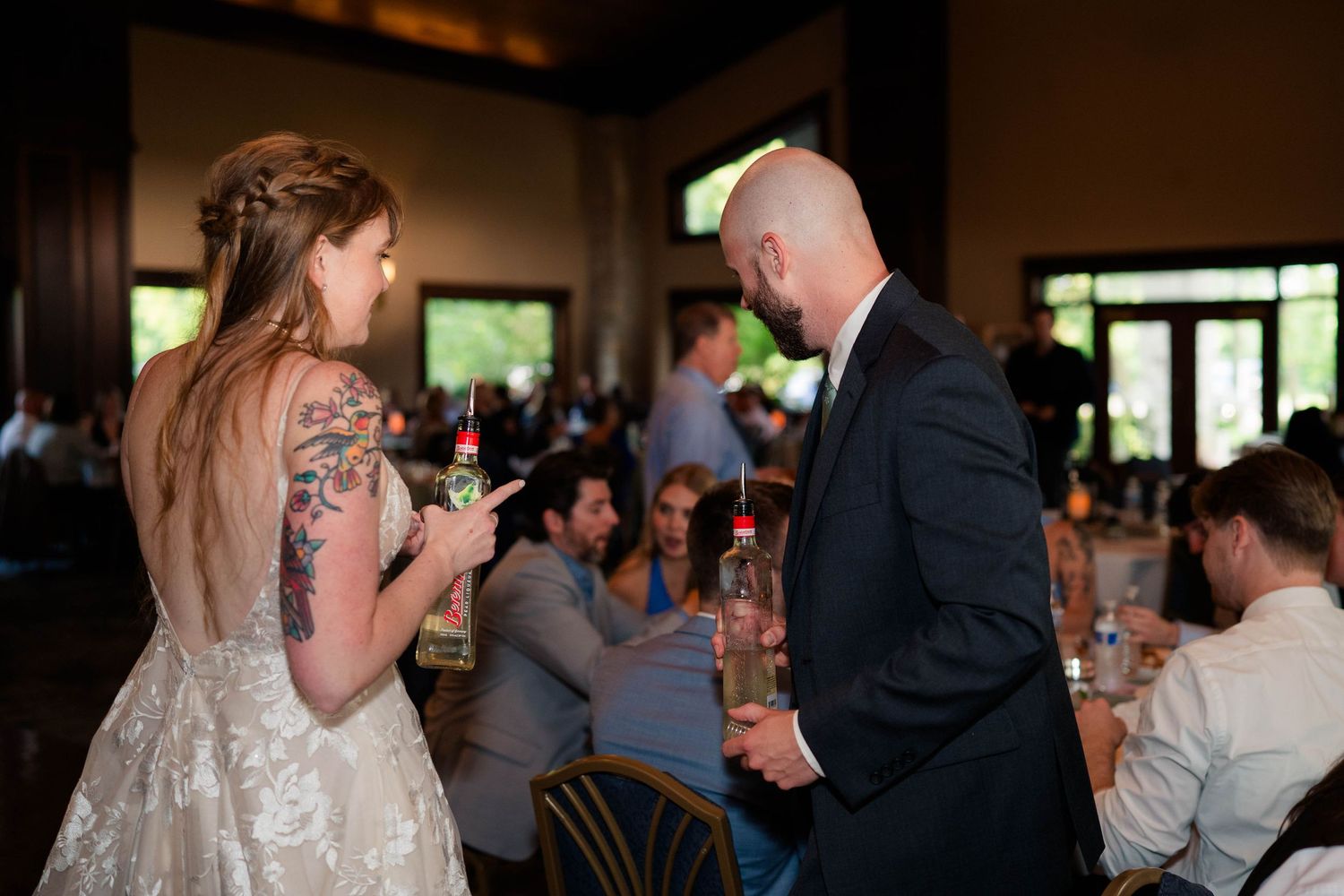Bride with tattoos and groom in black suit sharing a moment at wedding reception.