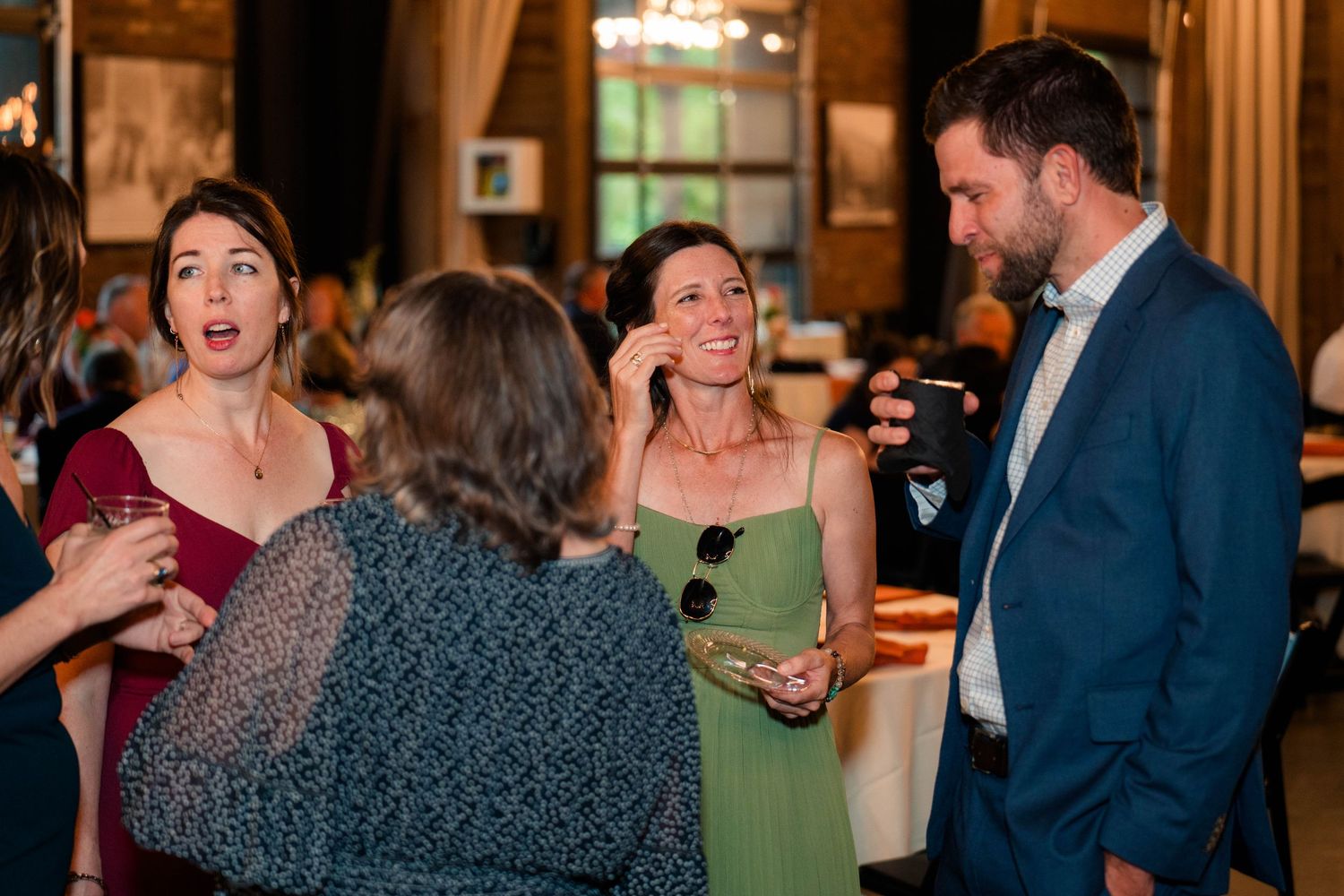 Wedding guests in formal attire laughing and socializing during reception in elegant venue.