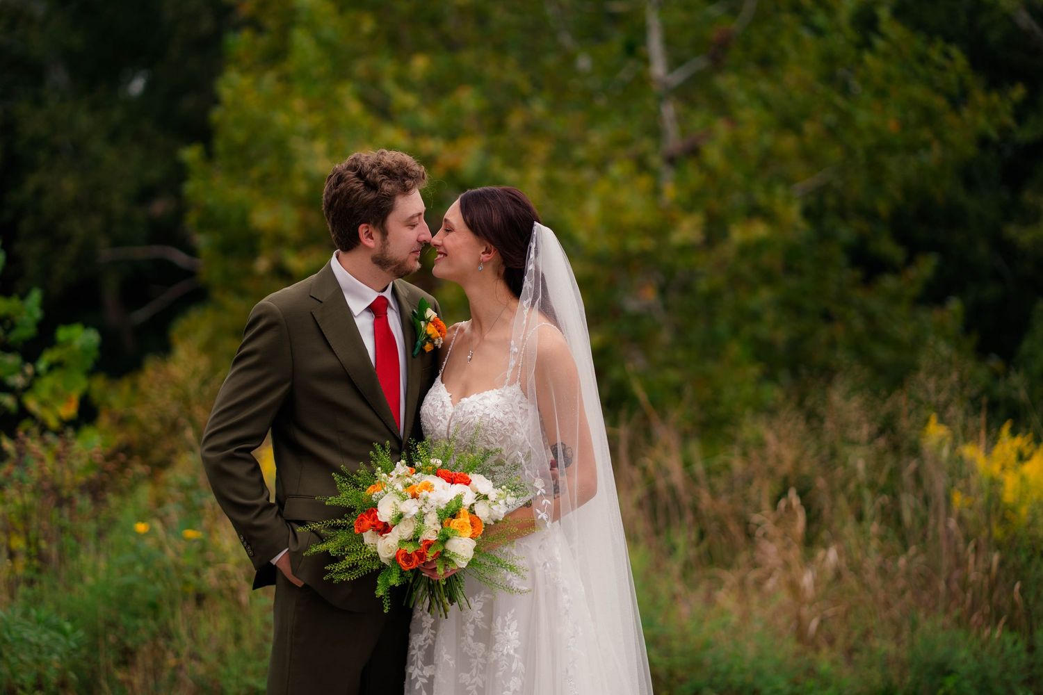 Bride and groom share a romantic moment in a lush outdoor setting, bride holding a vibrant bouquet.