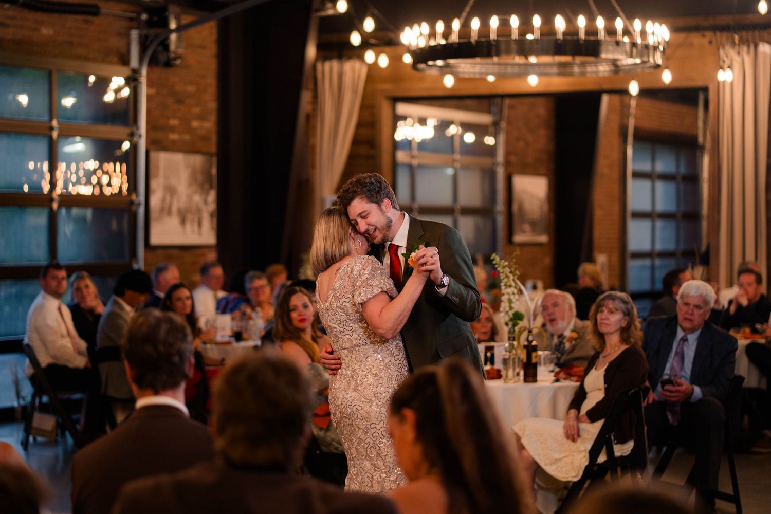 Couple sharing a romantic first dance at their wedding reception surrounded by guests in a warmly lit venue.