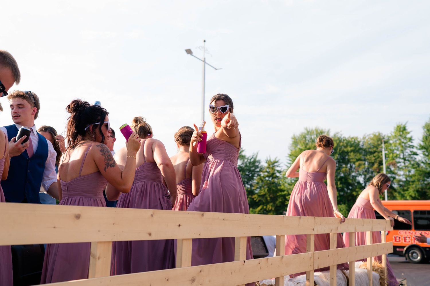 Bridesmaids in purple dresses celebrate at outdoor wedding reception on sunny day.
