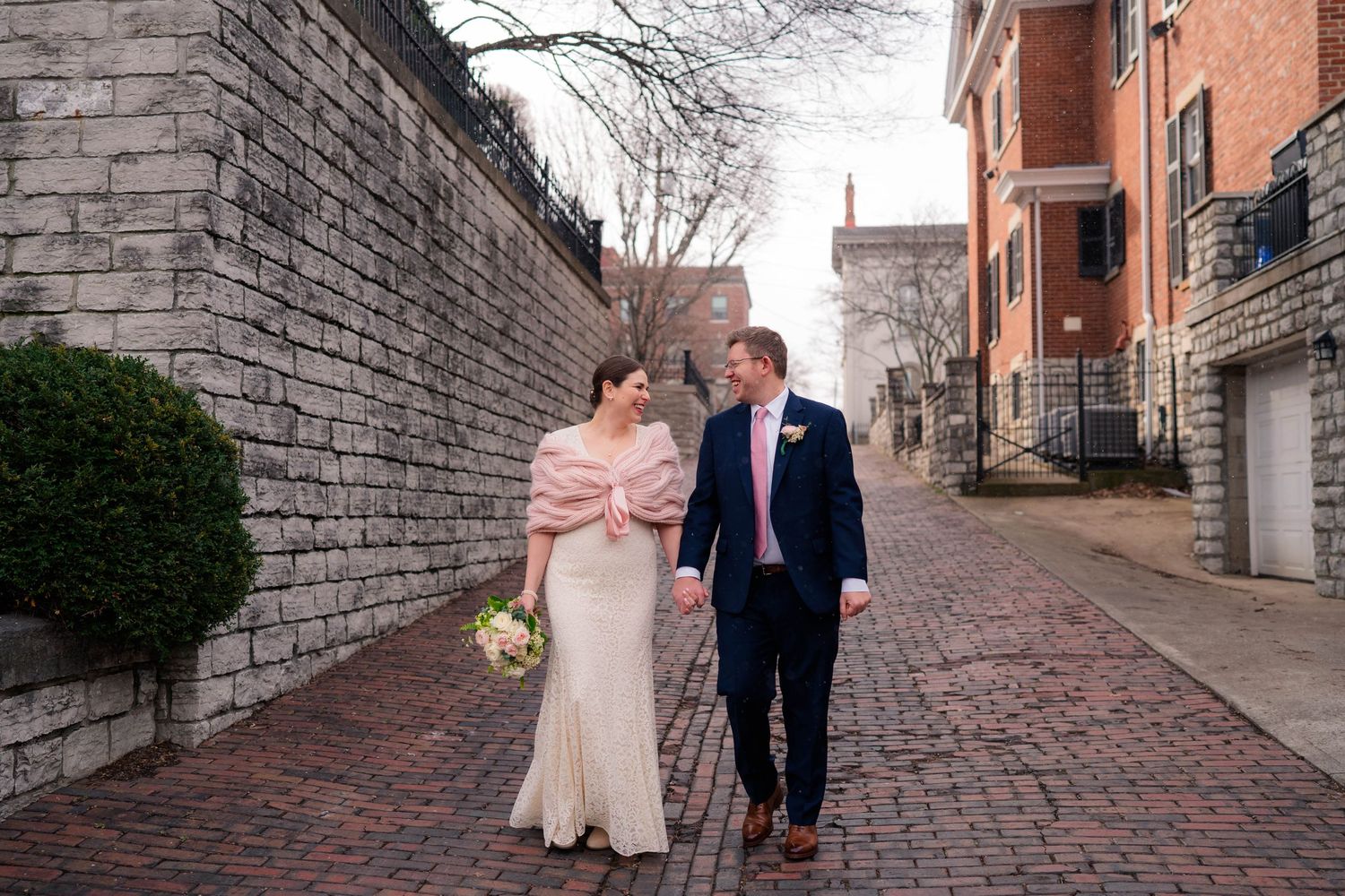 Newlyweds stroll along a charming brick alleyway lined with stone walls and historic buildings on their wedding day.