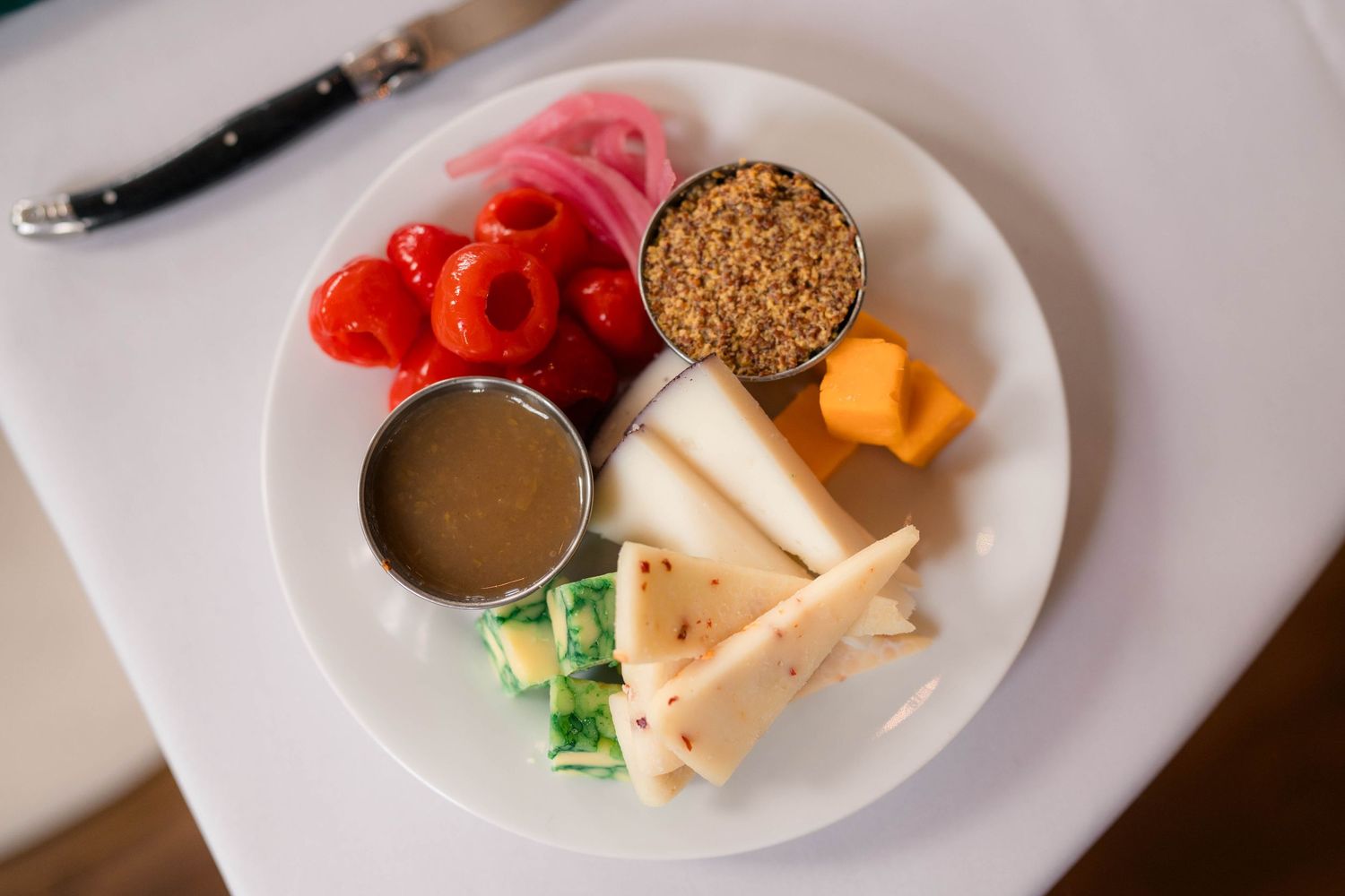 Artisan cheese and charcuterie plate with pickled vegetables, crackers, and dipping sauce on a white plate.
