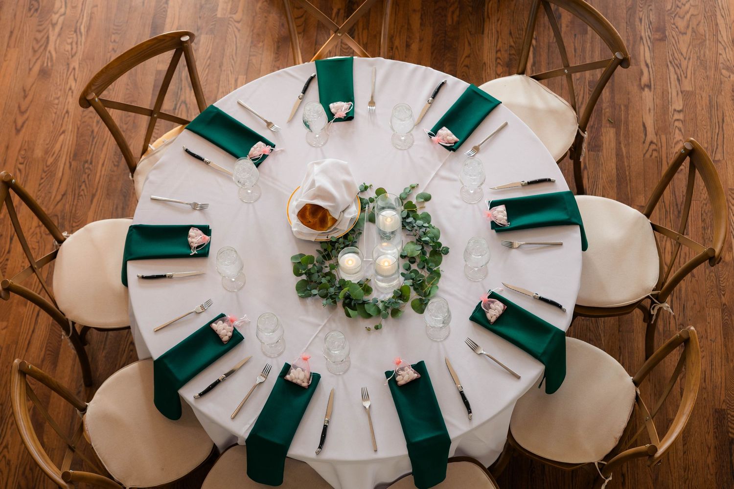 Bird's eye view of round wedding reception table with emerald green napkins, white linens, and greenery centerpiece.