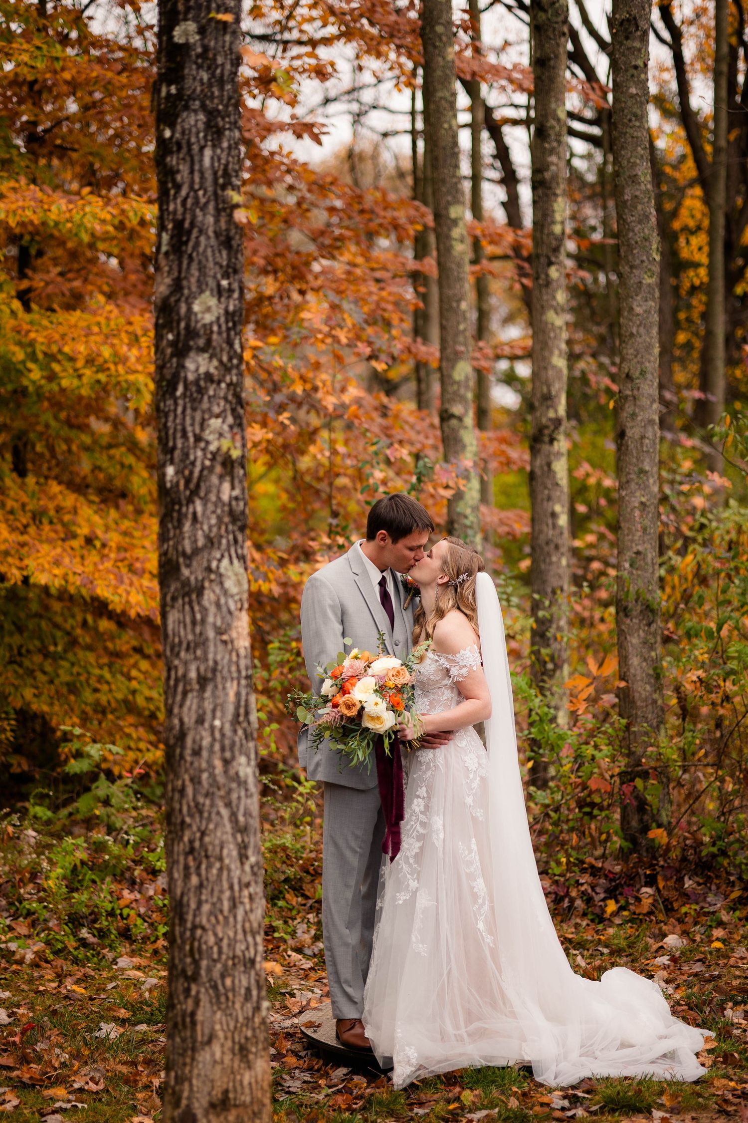 Couple sharing a romantic kiss in a forest surrounded by brilliant orange and red fall foliage.
