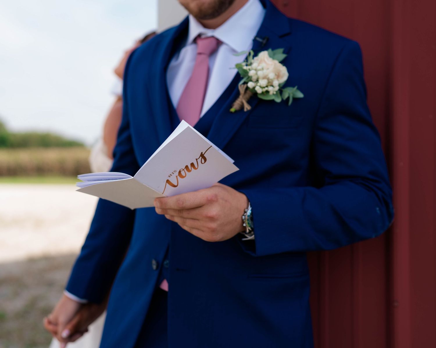 Groom in navy blue suit reading wedding vows from a booklet with floral boutonniere.