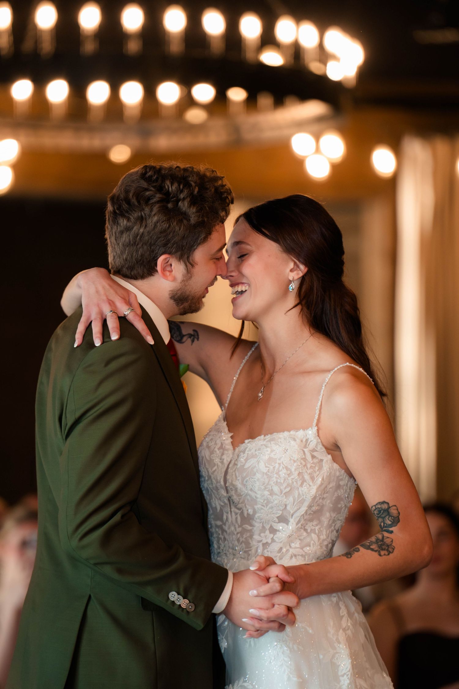 Smiling bride and groom share intimate first dance moment under glowing reception lights.