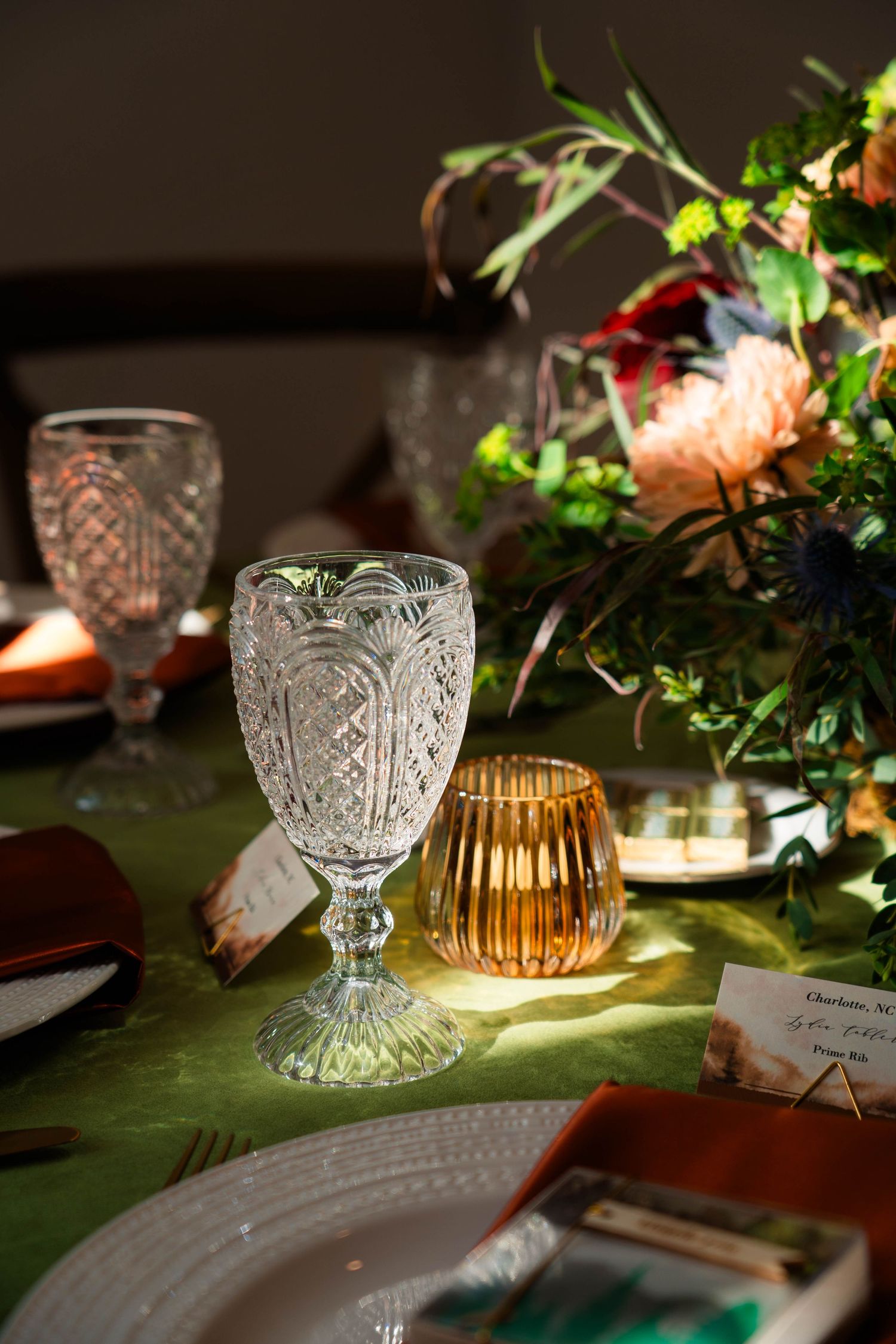 Elegant crystal goblet and amber candle holder on a green linen reception table.