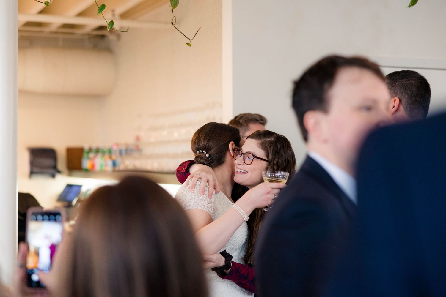 Bride hugging a wedding guest while holding a champagne glass at the reception.