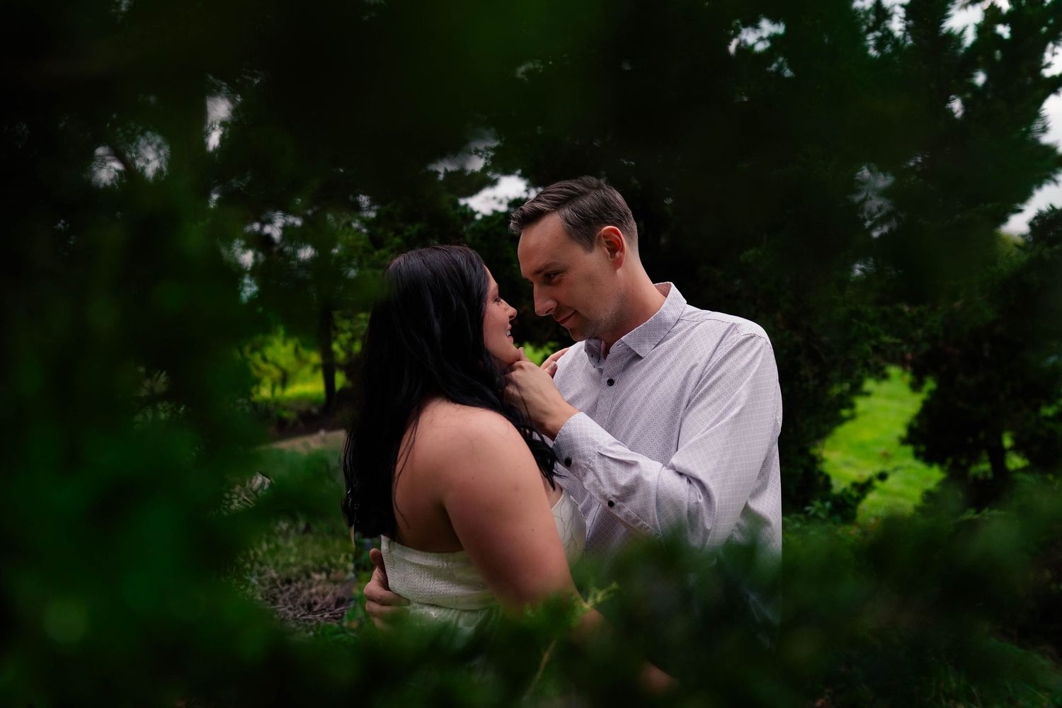 An engaged couple shares an intimate moment surrounded by lush green foliage during their outdoor photo session.
