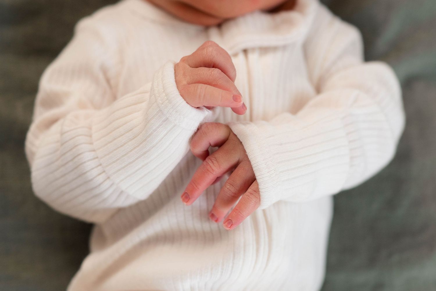 Close-up of newborn baby hands clasped together in white ribbed onesie.