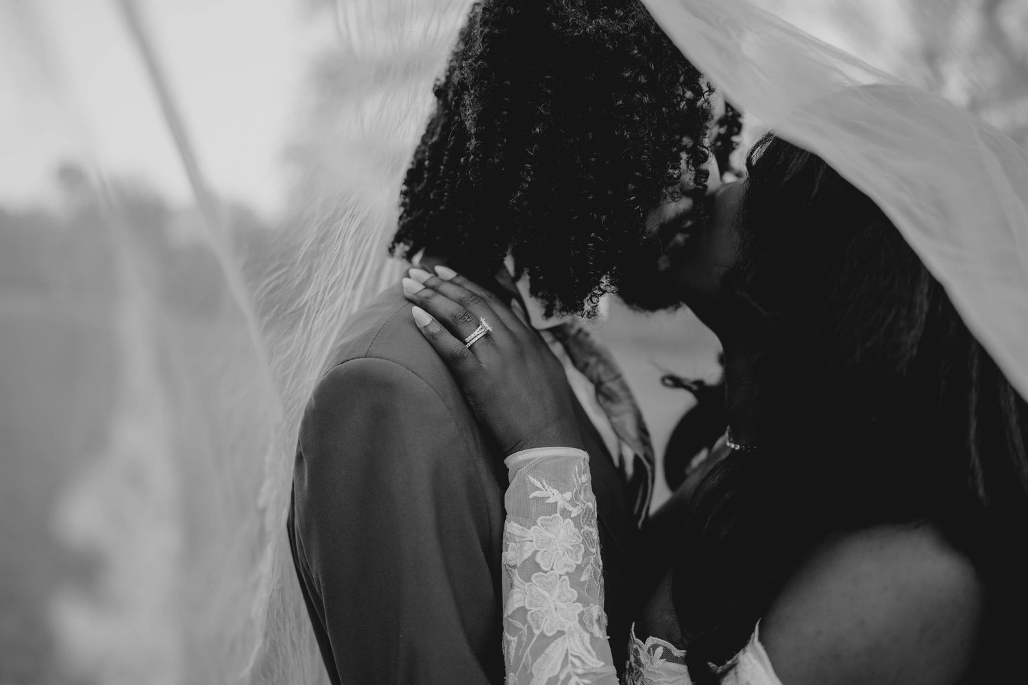 Black and white wedding photo of couple sharing romantic kiss under bridal veil.