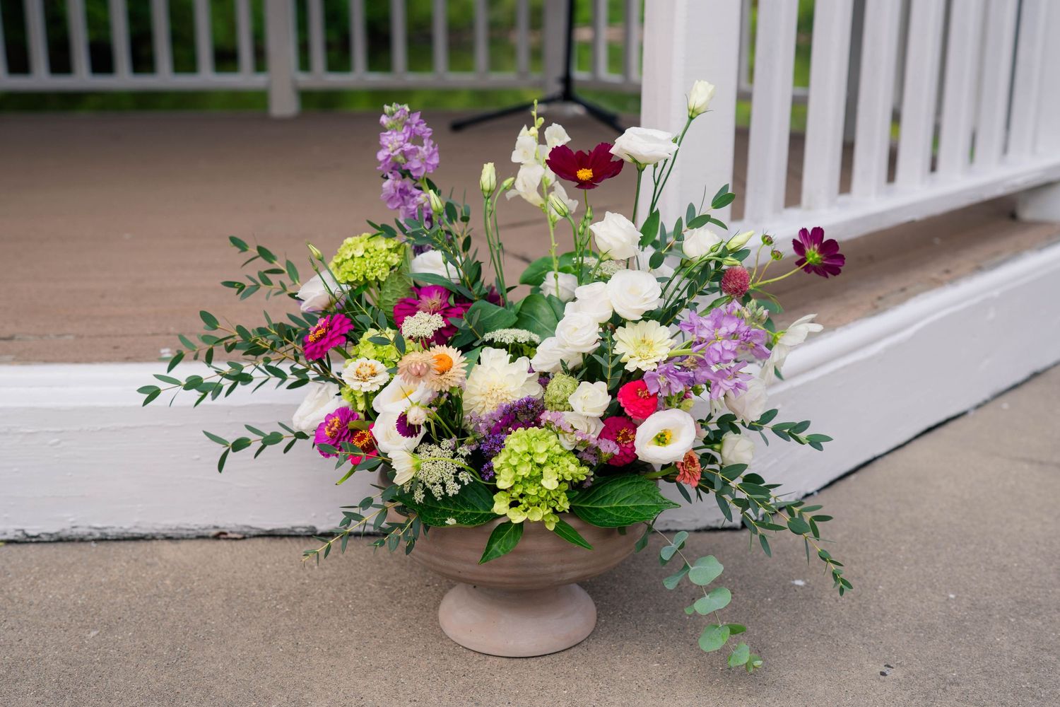 Colorful floral arrangement in a pedestal vase on a porch at a wedding venue.