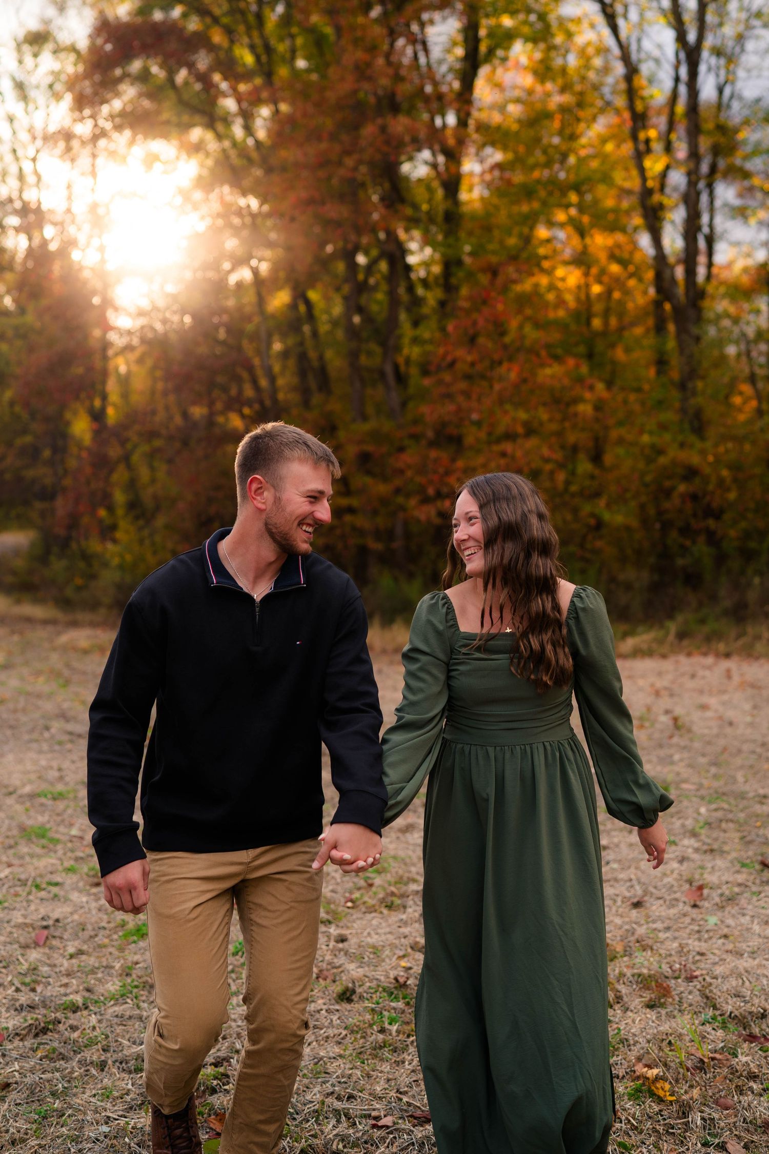 Happy couple holding hands and laughing while walking in an autumn meadow at sunset.