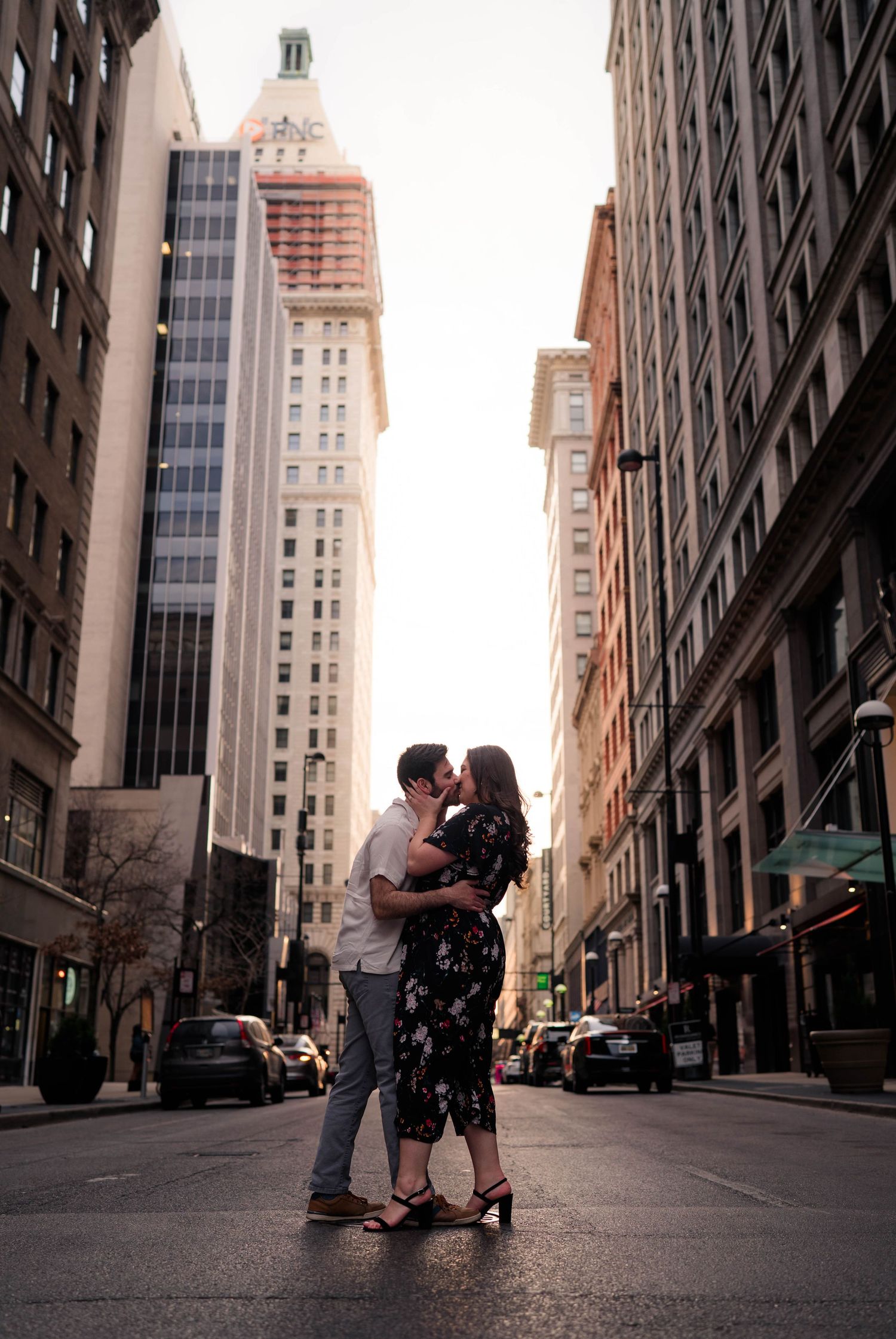 Couple sharing a romantic kiss in the middle of a city street surrounded by tall buildings.