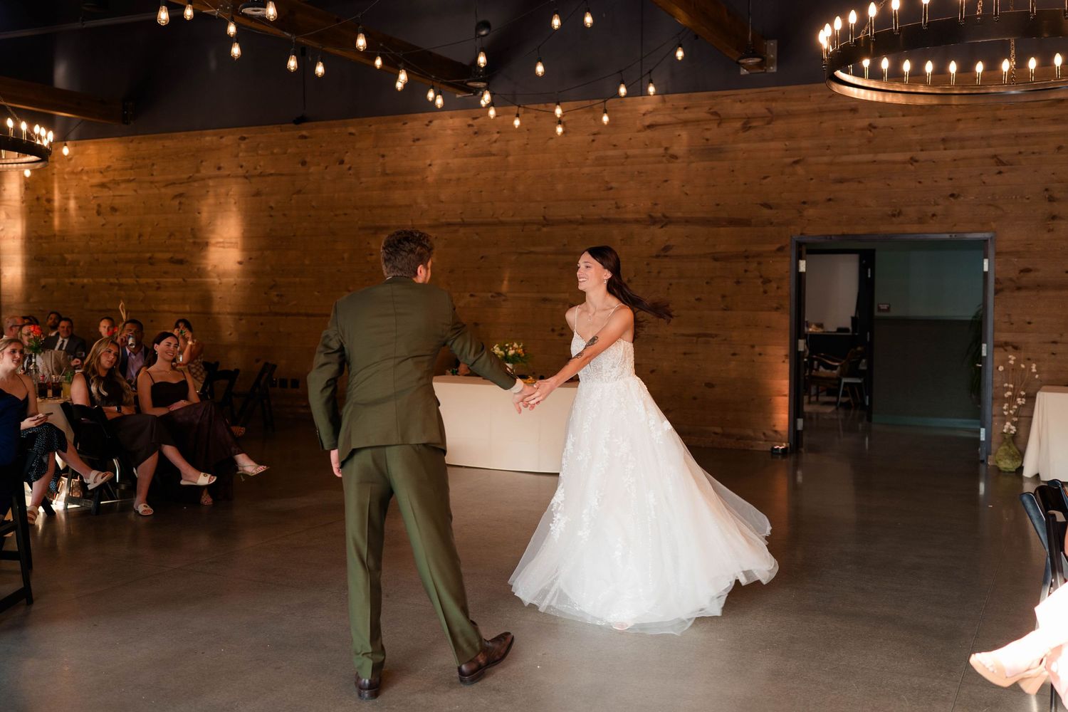 Bride and groom share their first dance in a warmly lit reception hall with string lights.