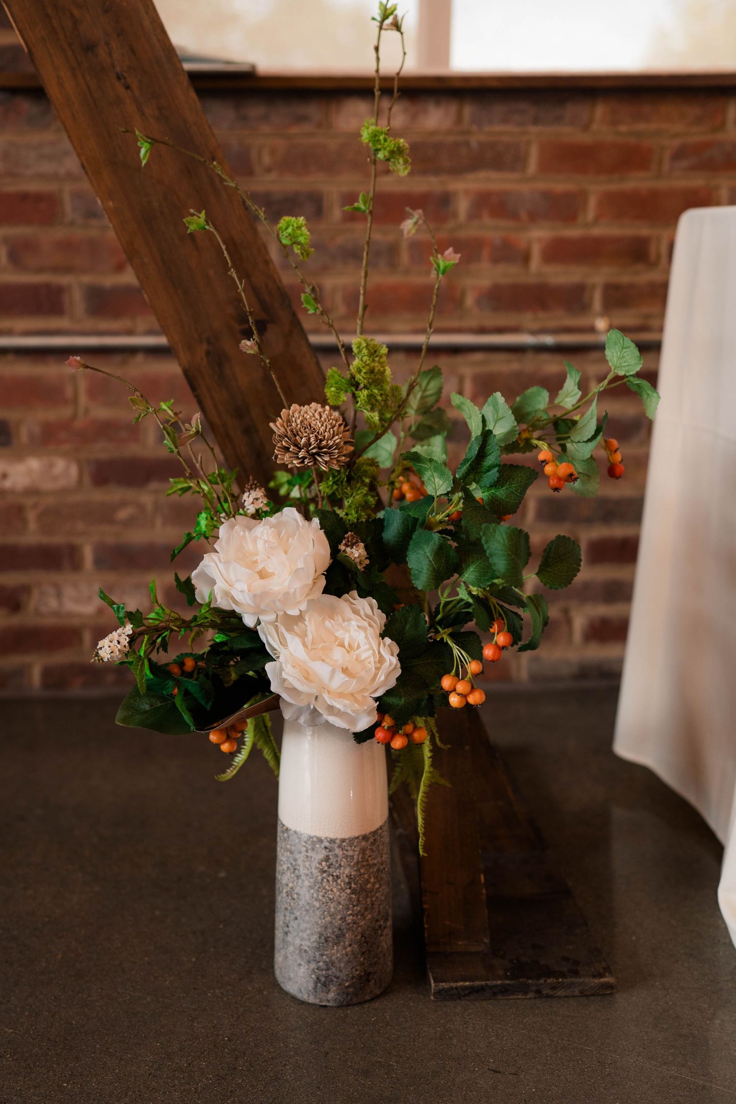 Elegant wedding floral arrangement with white peonies and orange berries in a vase.