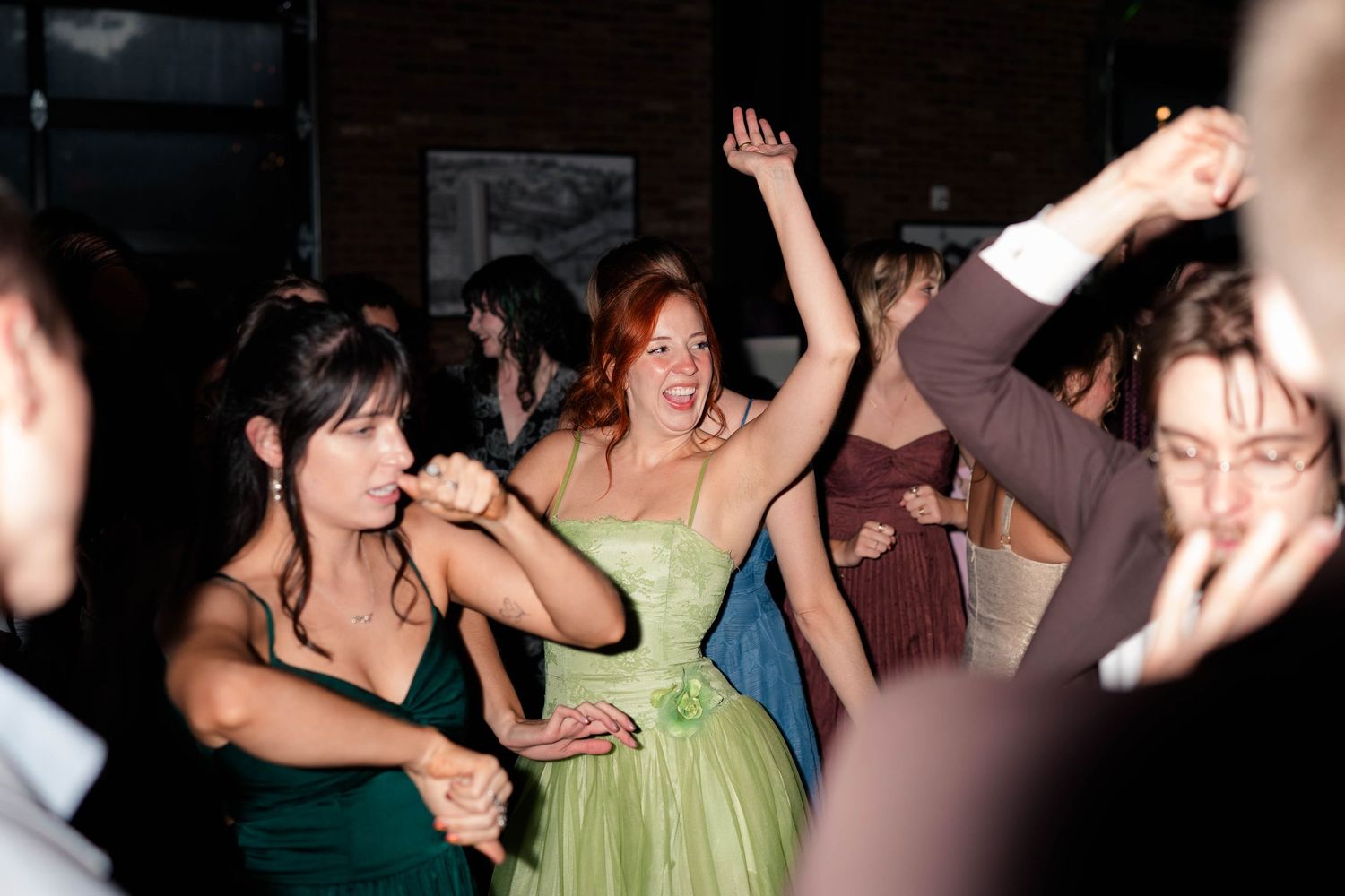 Wedding guests in colorful formal gowns dance joyfully on the reception dance floor.