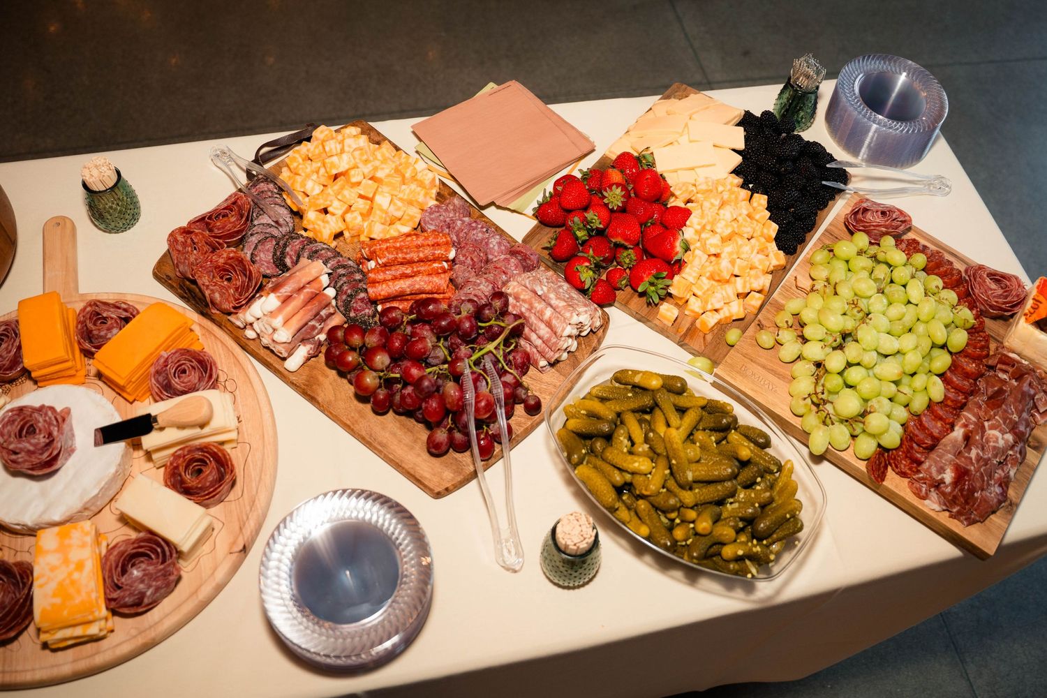 Wedding charcuterie spread featuring cheeses, meats, strawberries, grapes, and pickles on wooden boards.