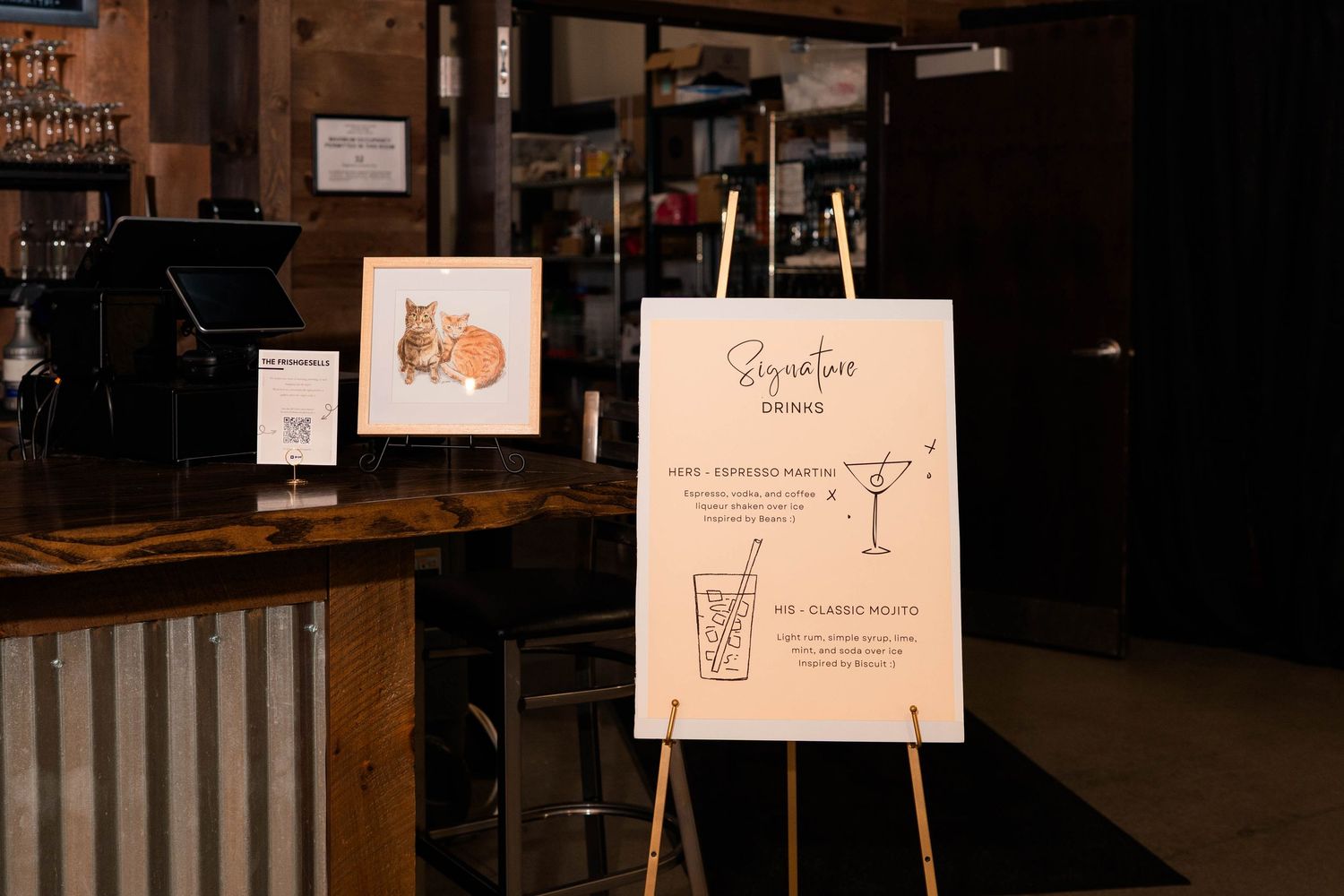 Wedding bar sign on easel displays signature cocktail menu with a decorative cat illustration.